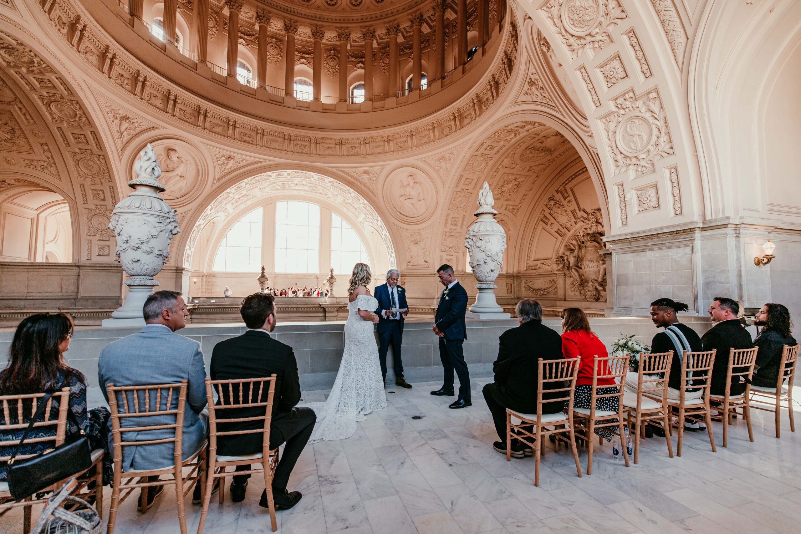 Wide ceremony view inside San Francisco City Hall’s Fourth Floor balcony with the couple exchanging vows under the historic dome, captured by a san francisco elopement photographer.
