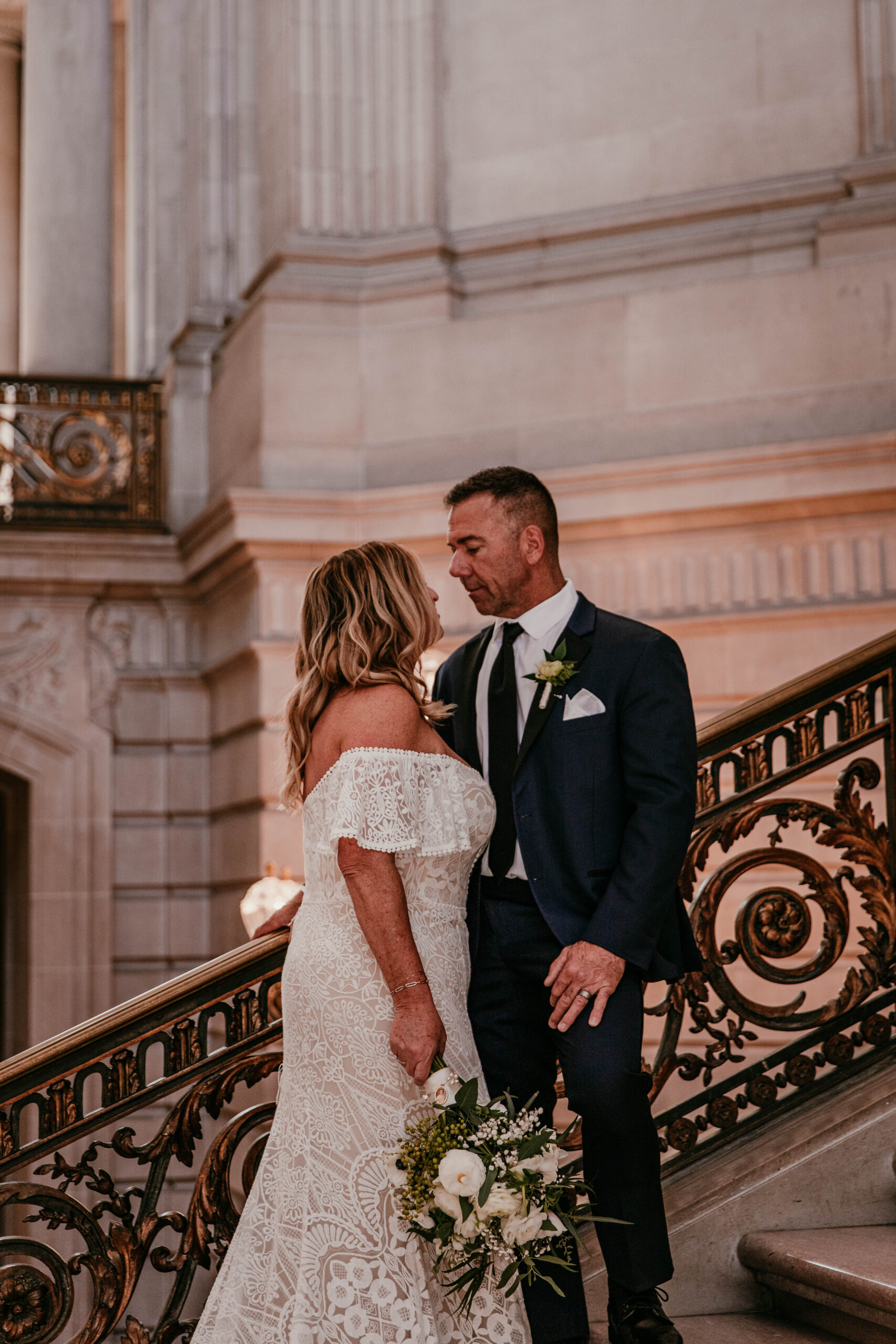 Bride and groom sharing a quiet moment on the staircase inside San Francisco City Hall during their elopement, photographed by a san francisco elopement photographer.