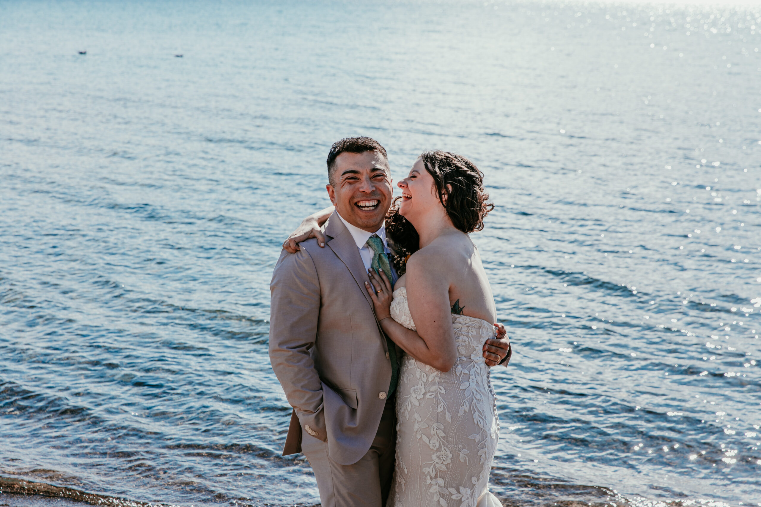 Couple laughing together during a Lake Tahoe California elopement, standing along the shoreline with clear blue water in the background