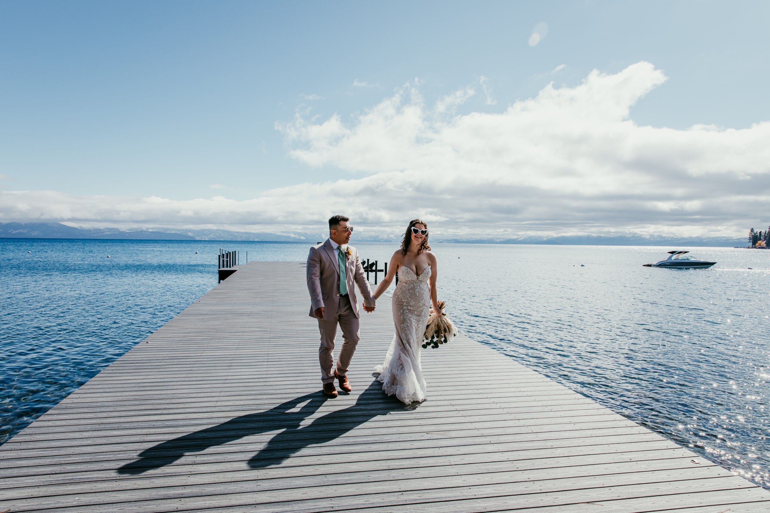 Couple walking hand in hand on a dock during a lakeside elopement, bride wearing a fitted lace elopement dress