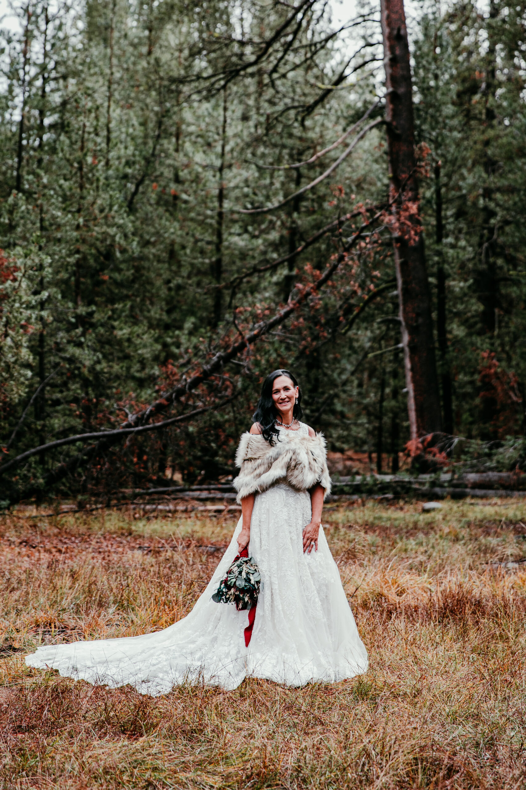 Bride wearing a lace elopement dress with a fur shawl during a fall forest elopement