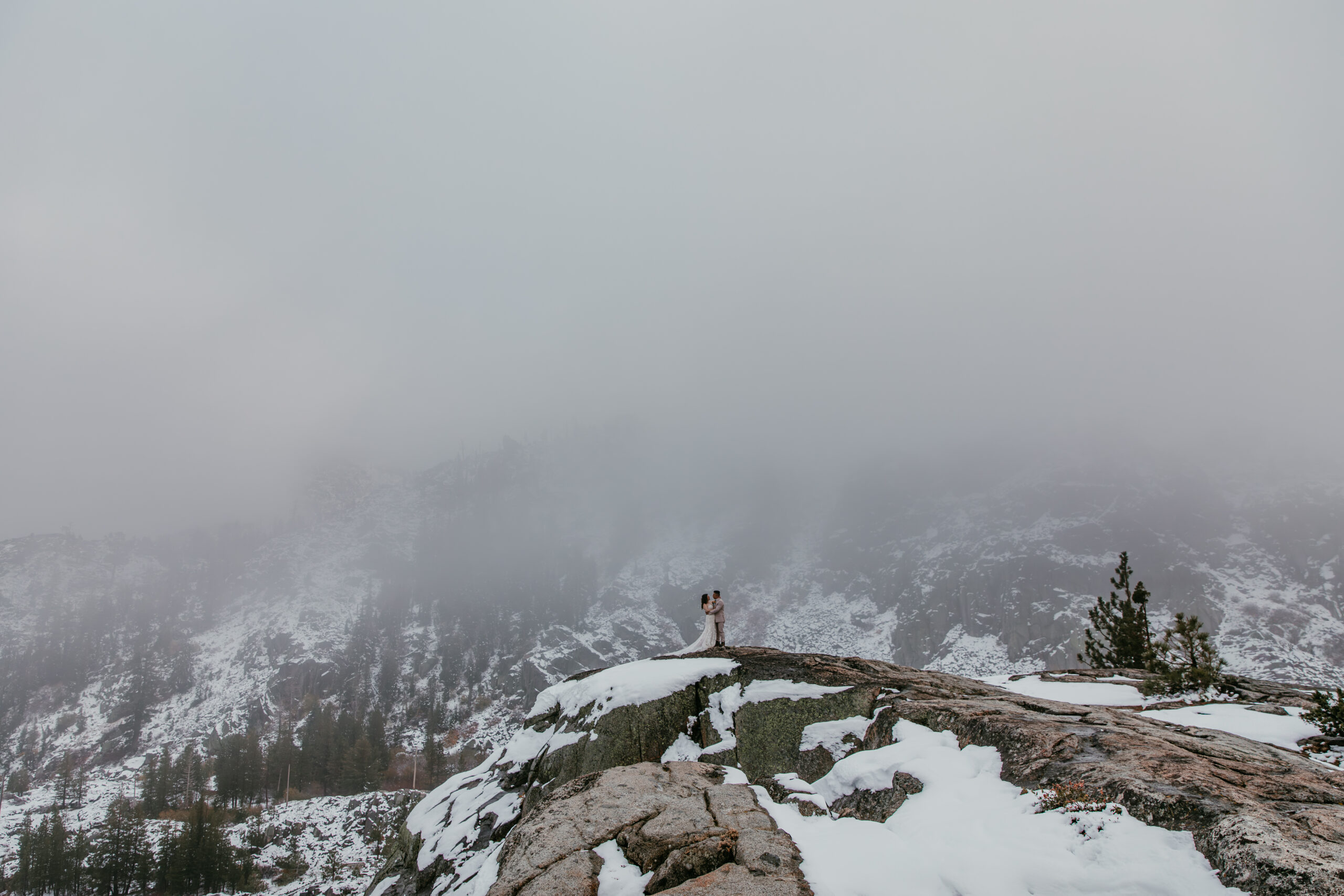 Bride and groom standing on a snowy cliff at Donner Summit surrounded by thick rolling fog.