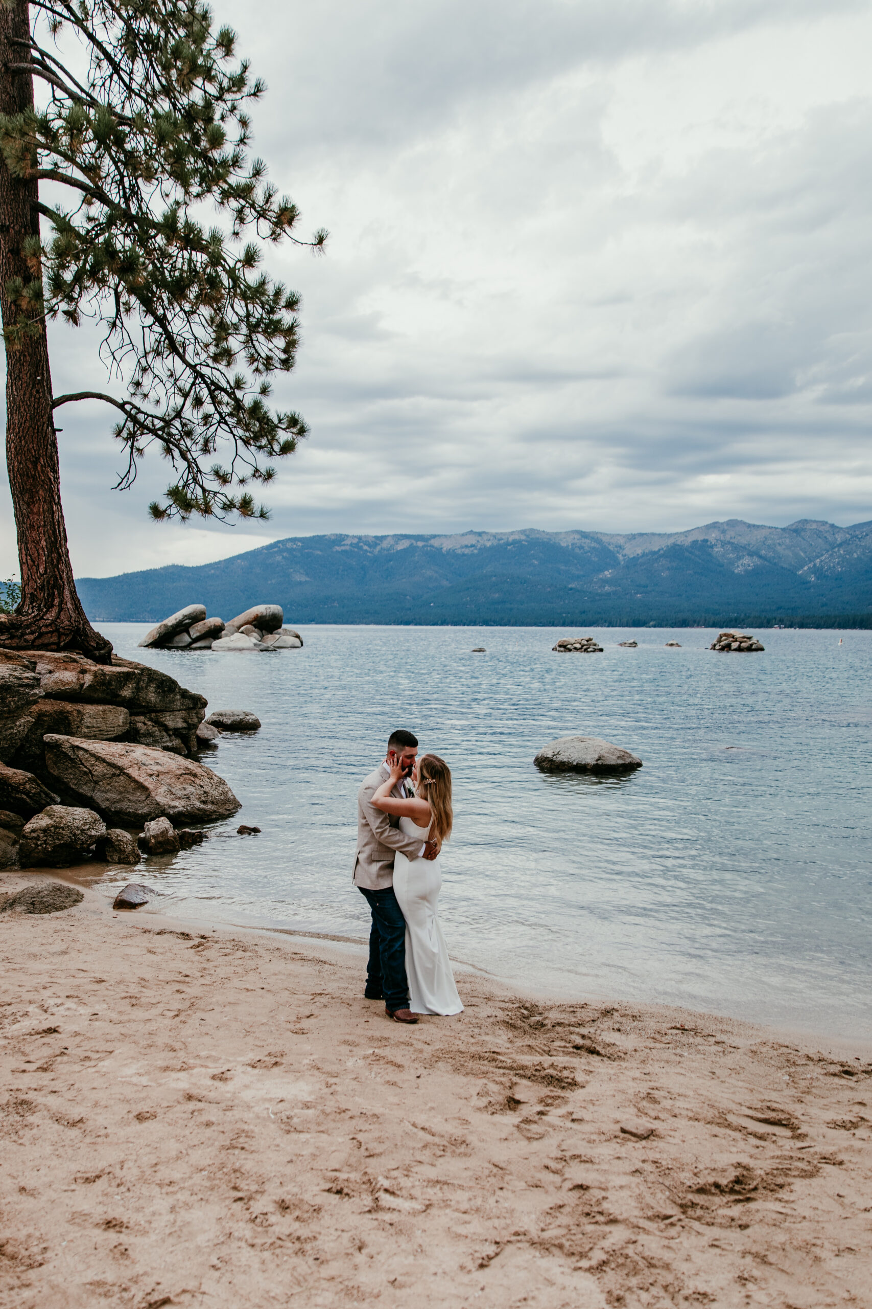 Lake Tahoe beach elopement couple embracing on sandy shore with pine trees and lake in Northern California