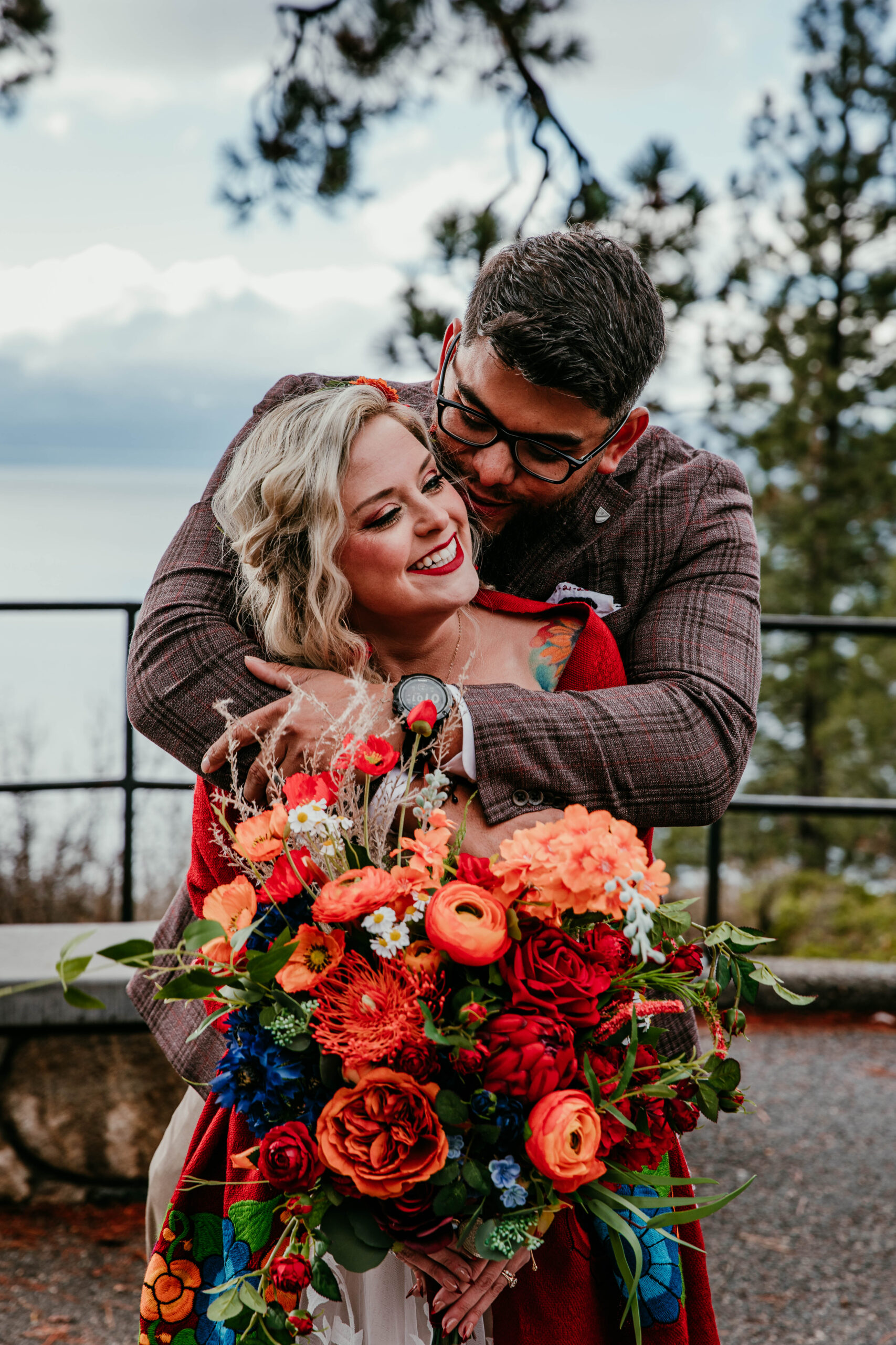 Bride and groom embracing during their winter elopement in Lake Tahoe with vibrant bouquet against snowy mountain backdrop.