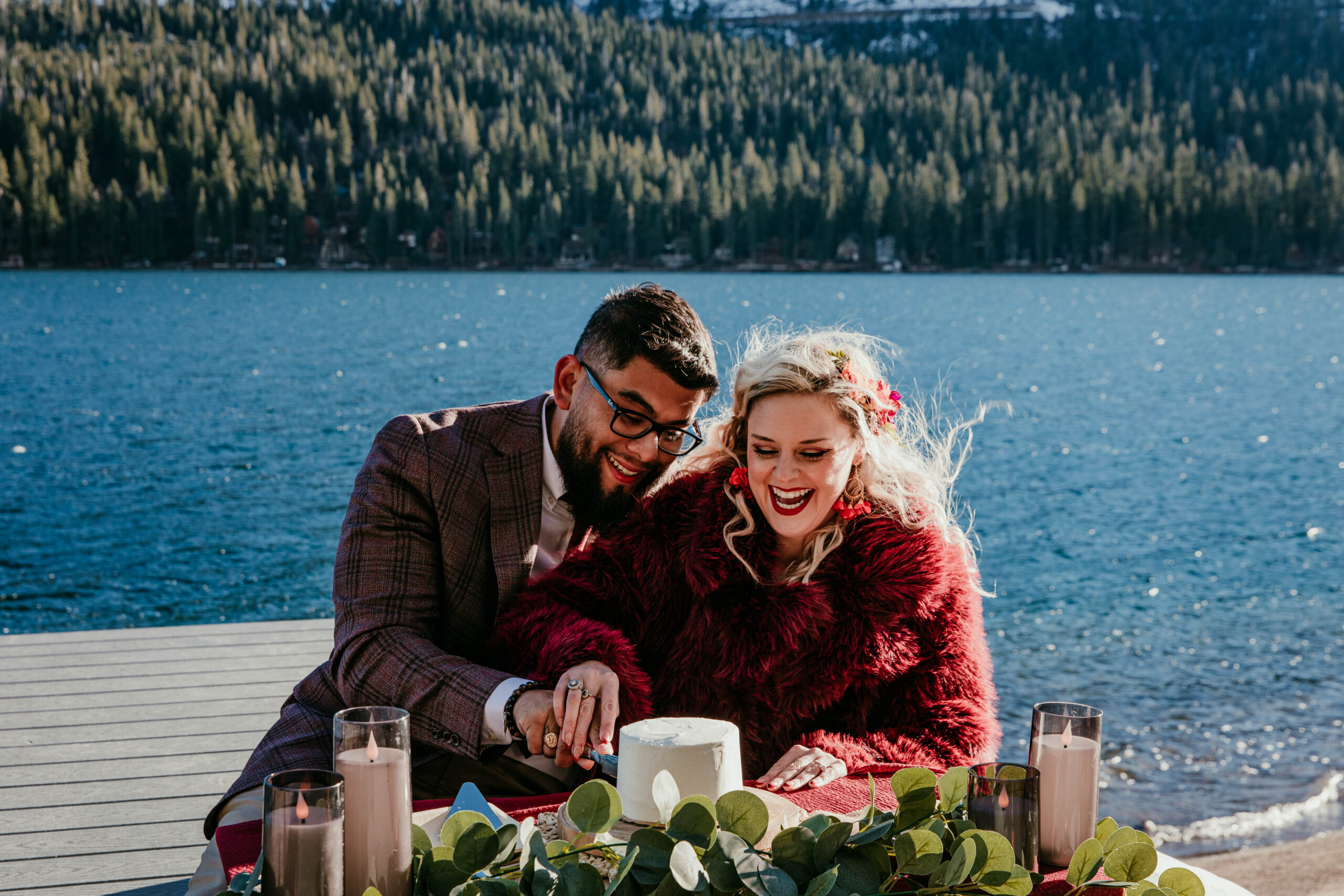 Couple cutting cake during their winter elopement at Donner Lake in Truckee with bright blue water and mountain backdrop.