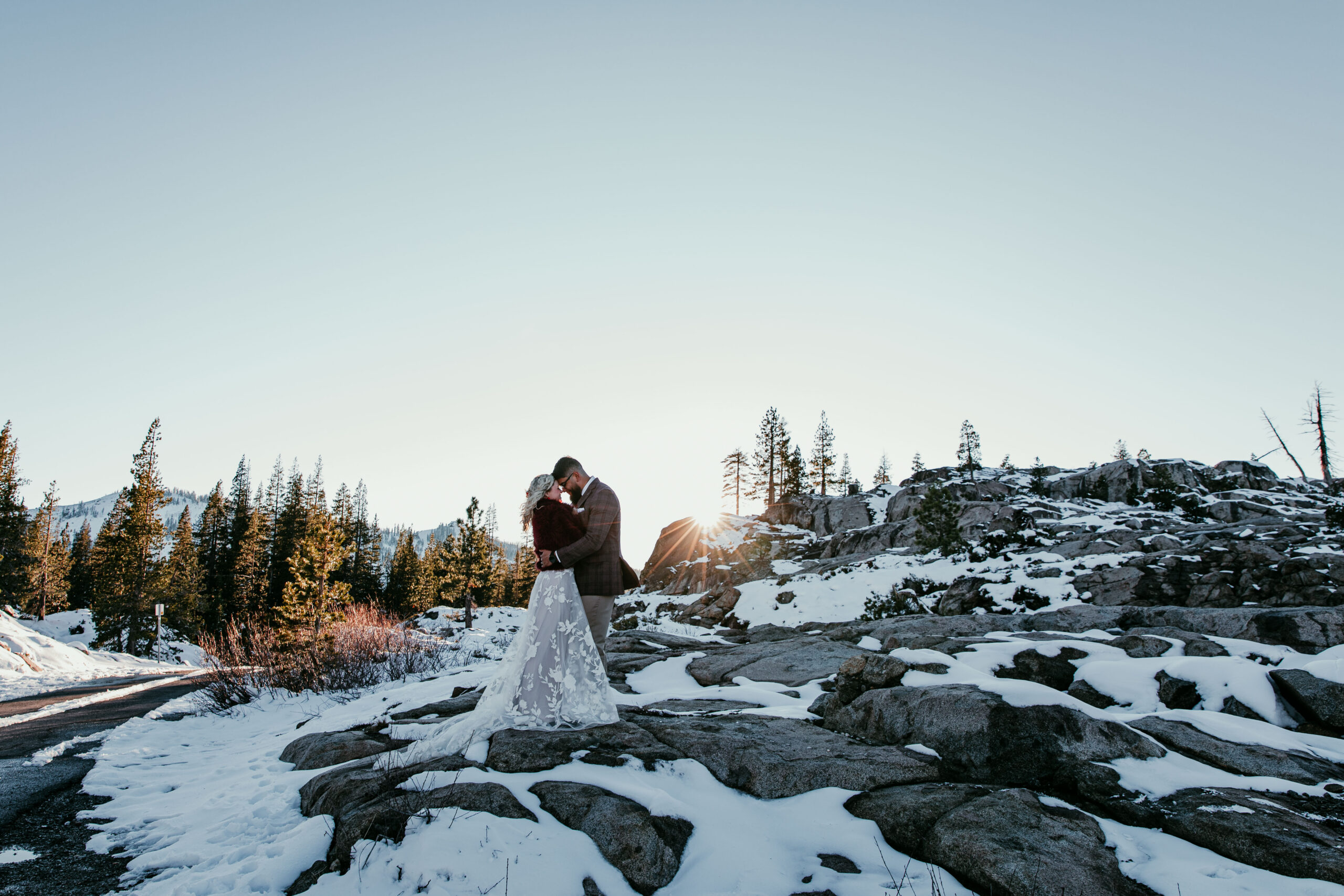 Couple embracing on snow-covered granite during sunset at Donner Summit in the Sierra Nevada.