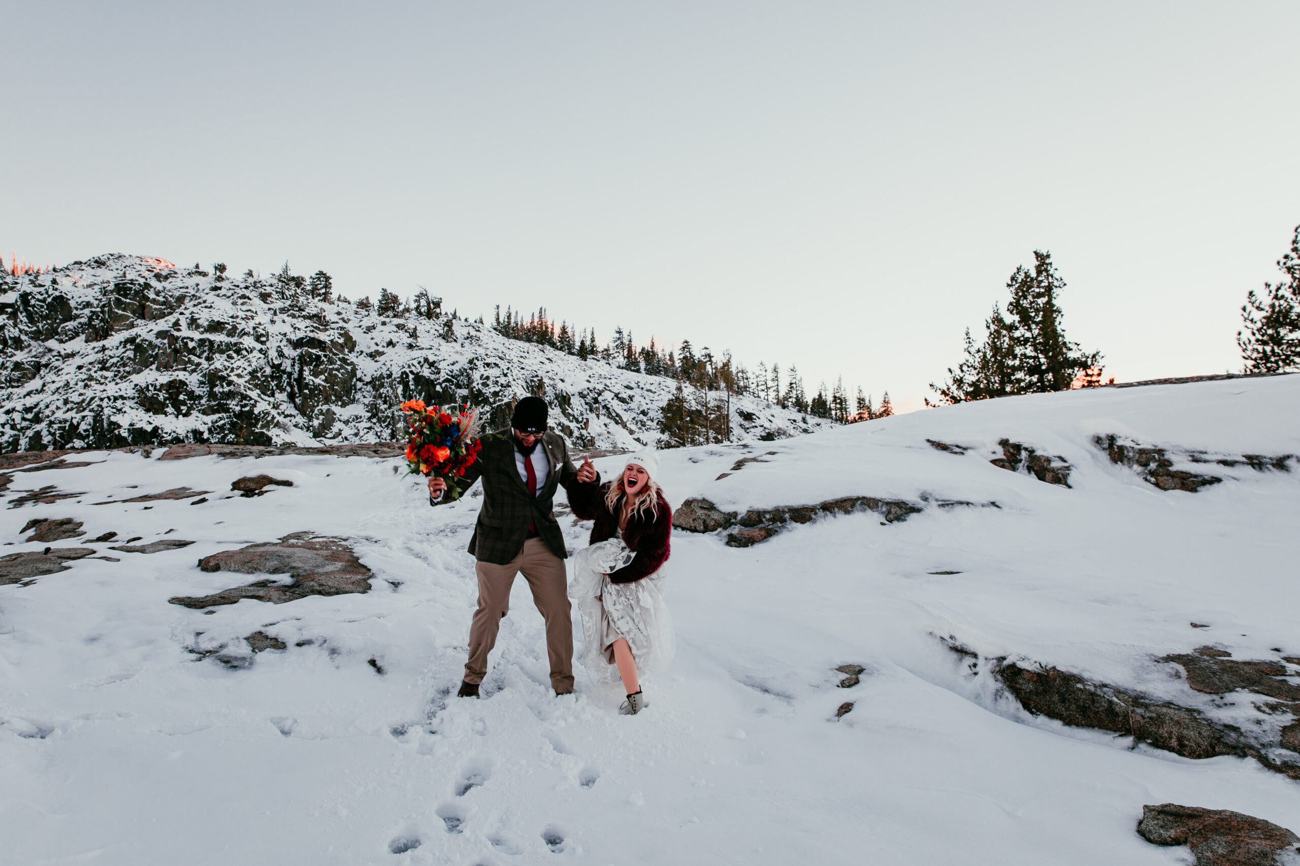 Bride holding vibrant bouquet while walking through fresh snow at Donner Summit during winter elopement portraits.