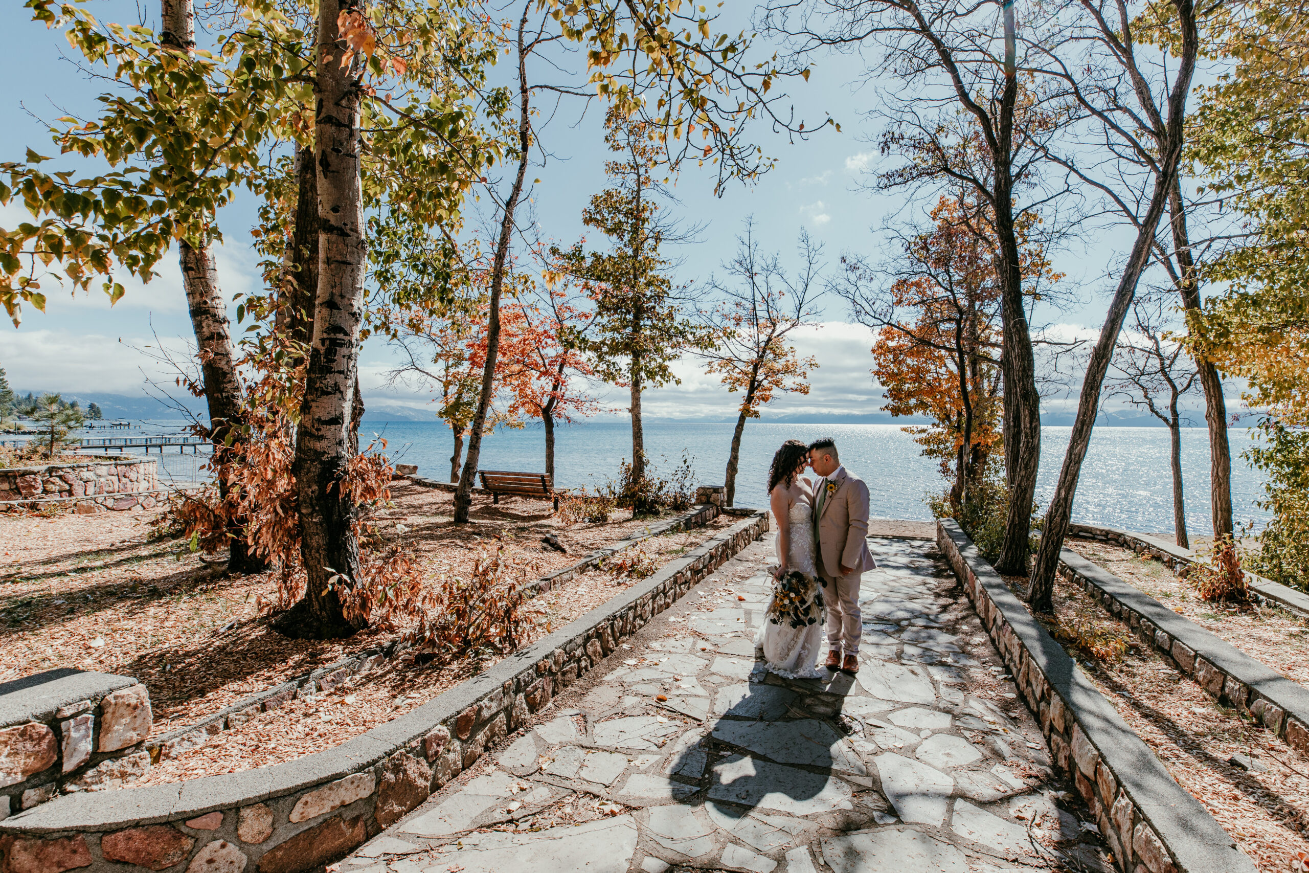 Bride and groom walking along a stone path lined with fall trees near Lake Tahoe in October.