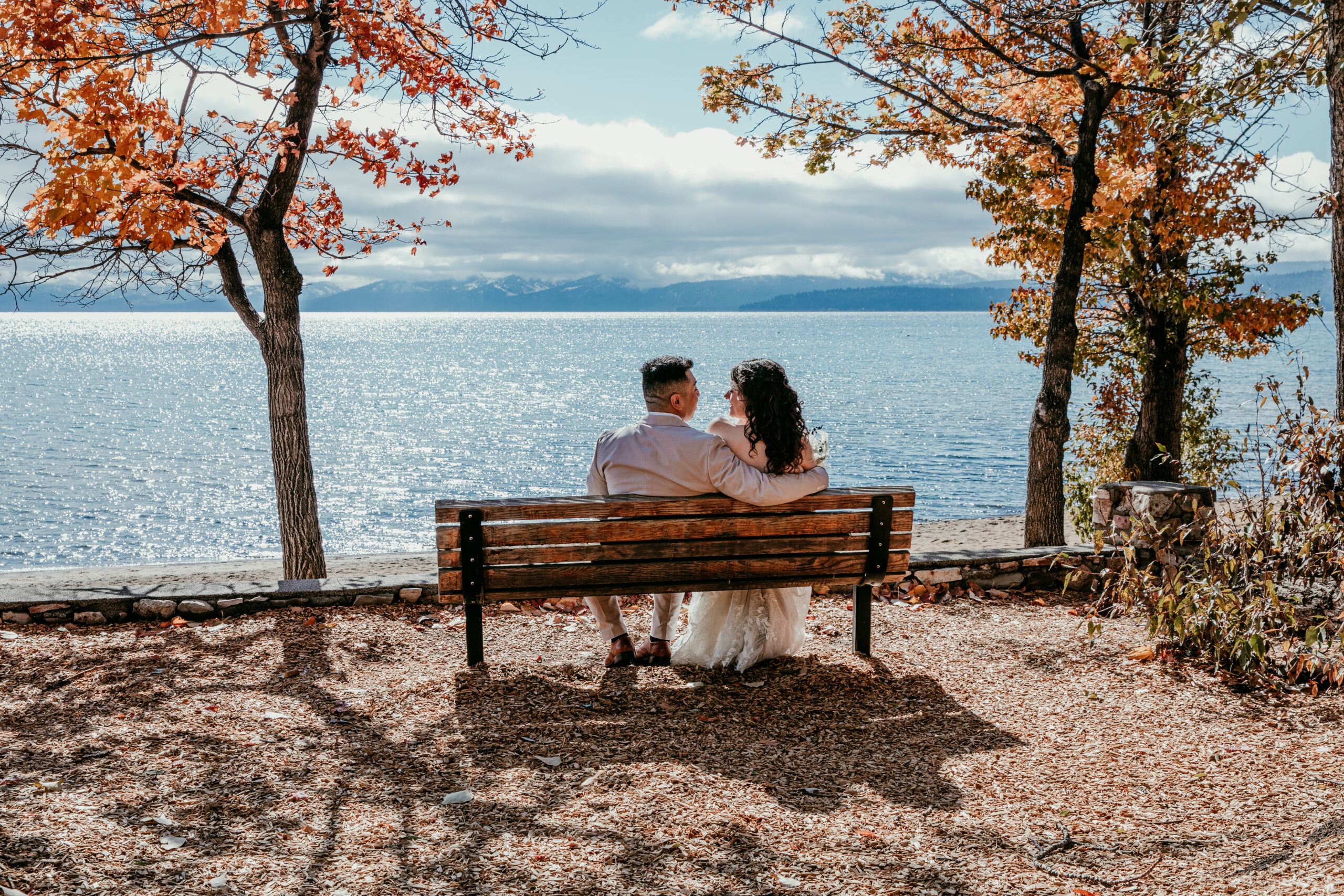 Couple sitting on a bench overlooking Lake Tahoe during a fall elopement with autumn colors