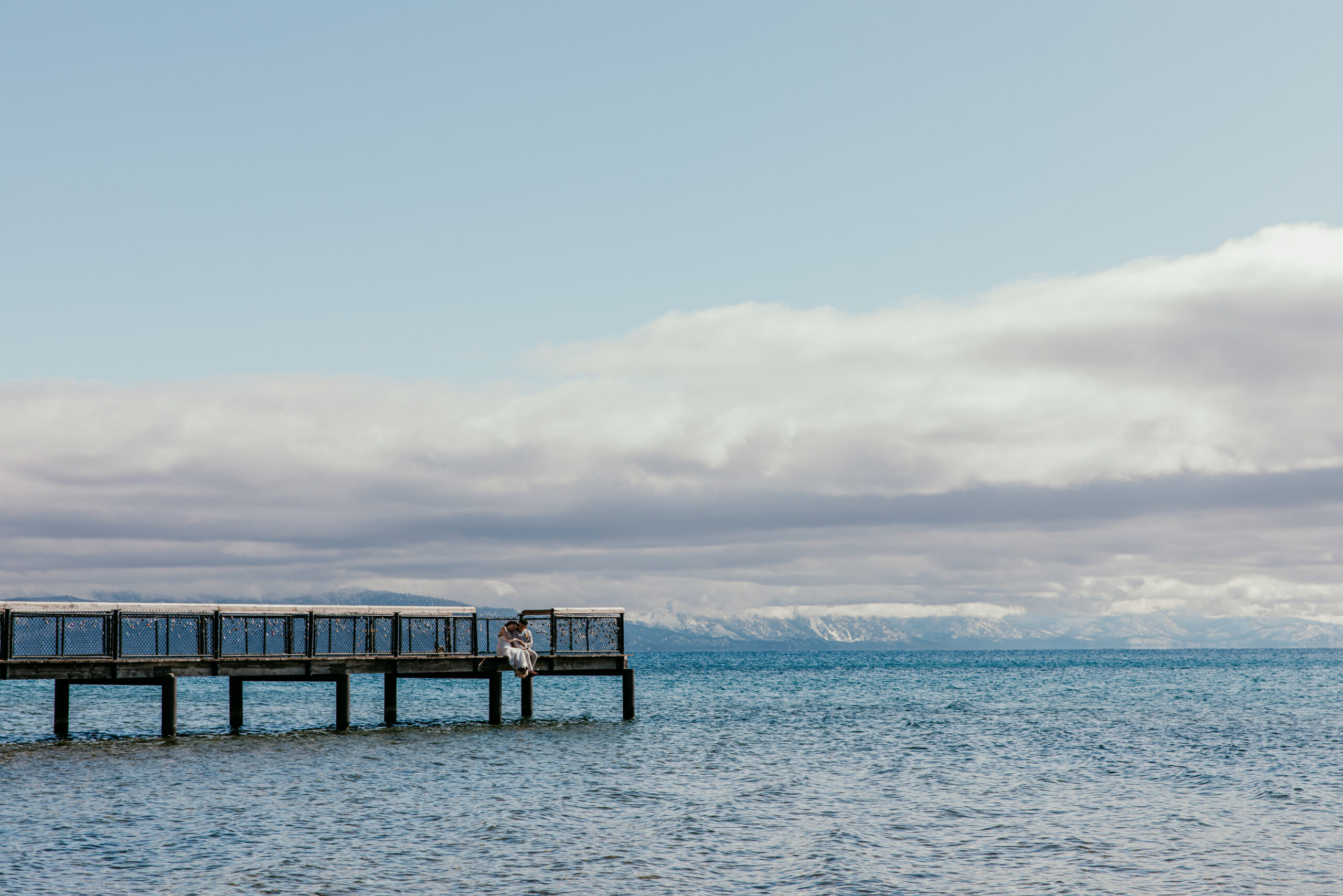 Wooden dock extending into Lake Tahoe with mountains and clouds in the distance.