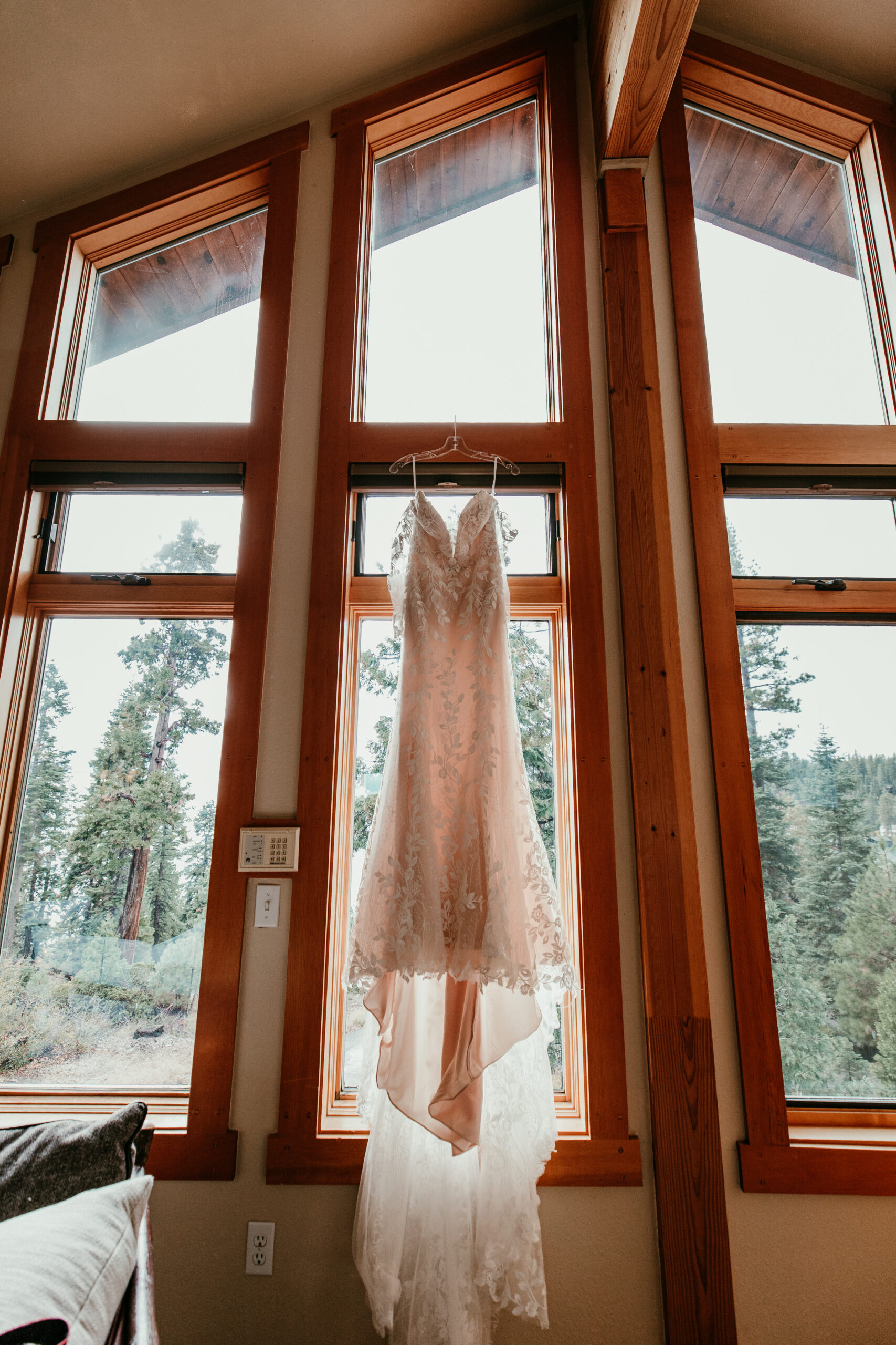 Wedding dress hanging in tall wood-framed windows inside a Lake Tahoe Airbnb before the October ceremony.