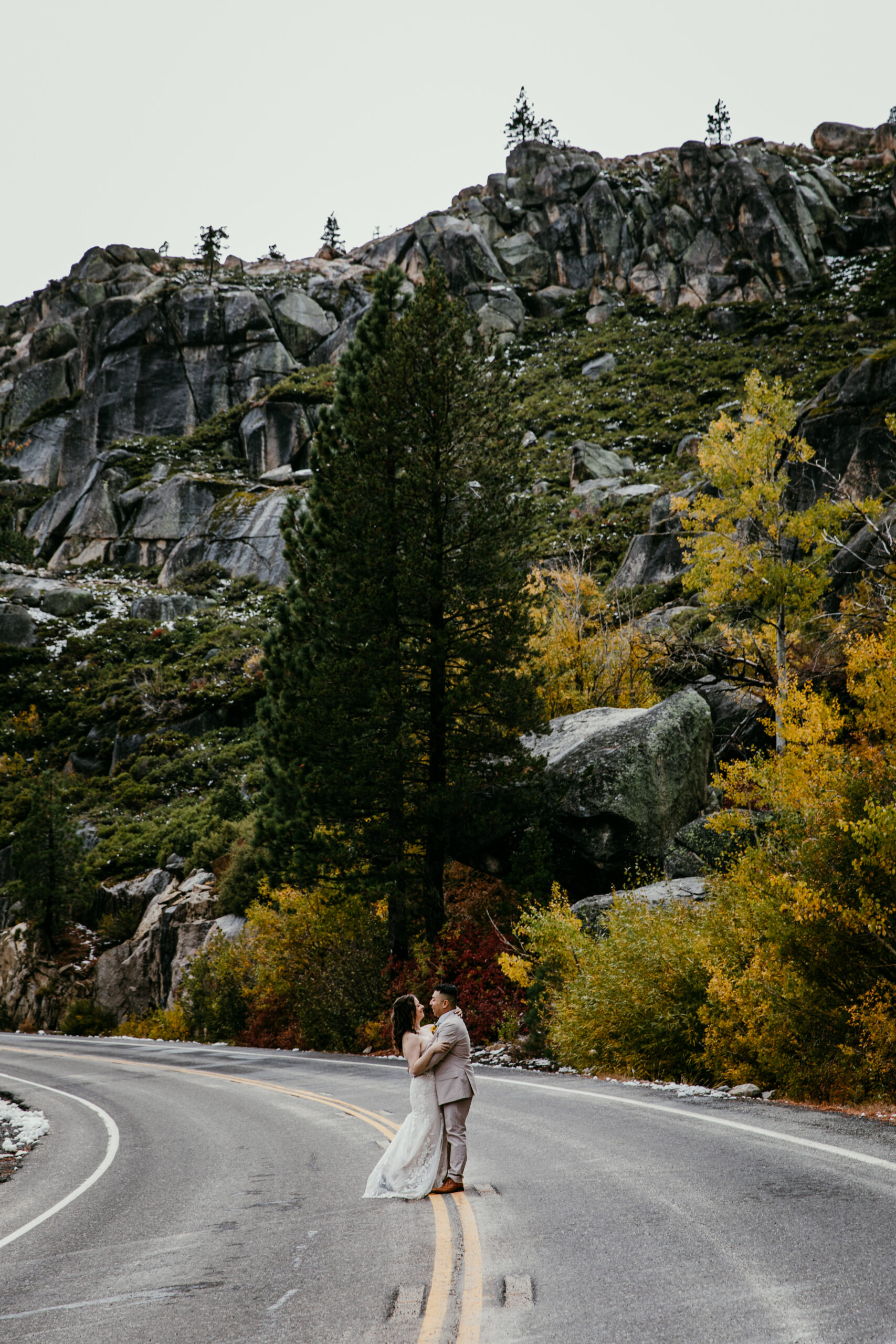 Bride and groom standing on a scenic mountain highway near Truckee with fall aspens and granite cliffs.