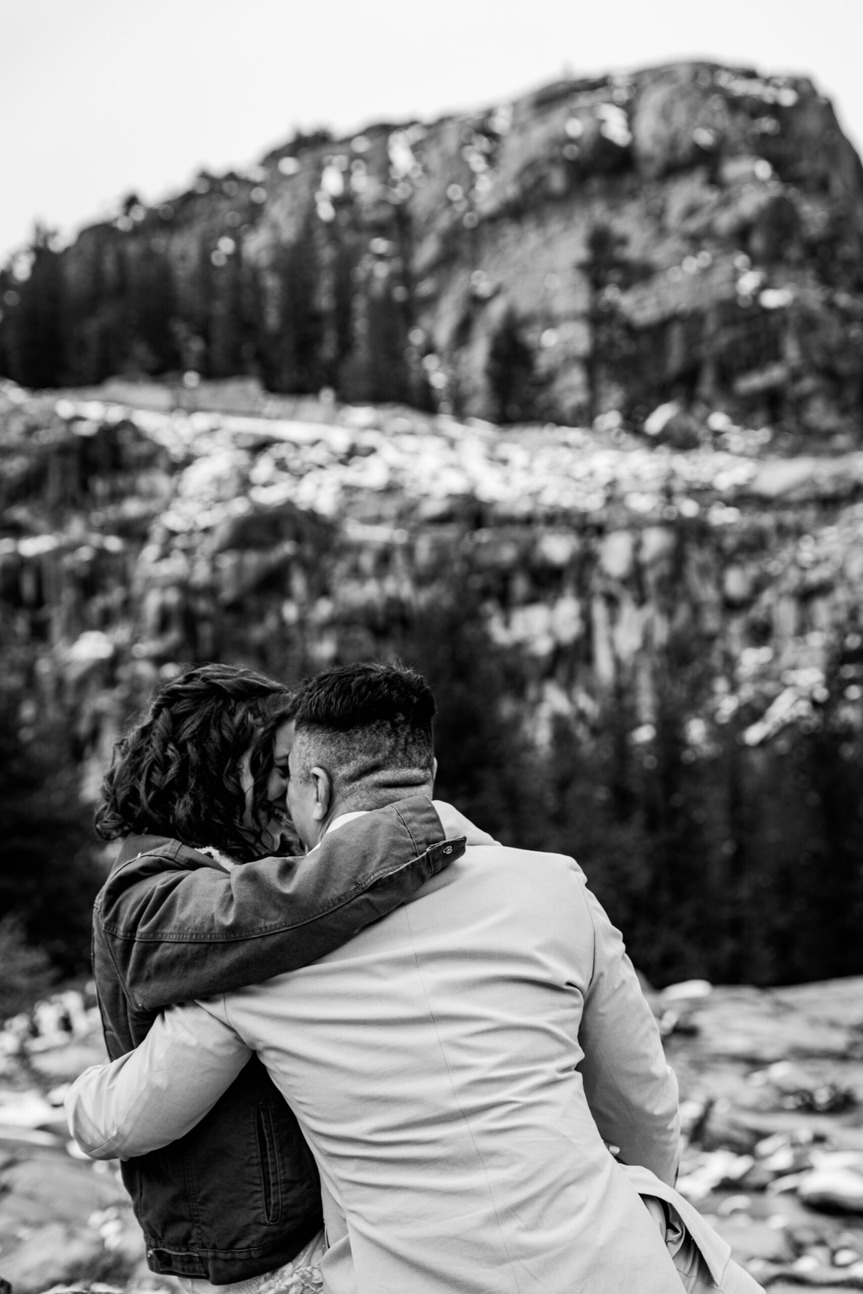 Black and white portrait of bride and groom embracing on a snowy mountain overlook.