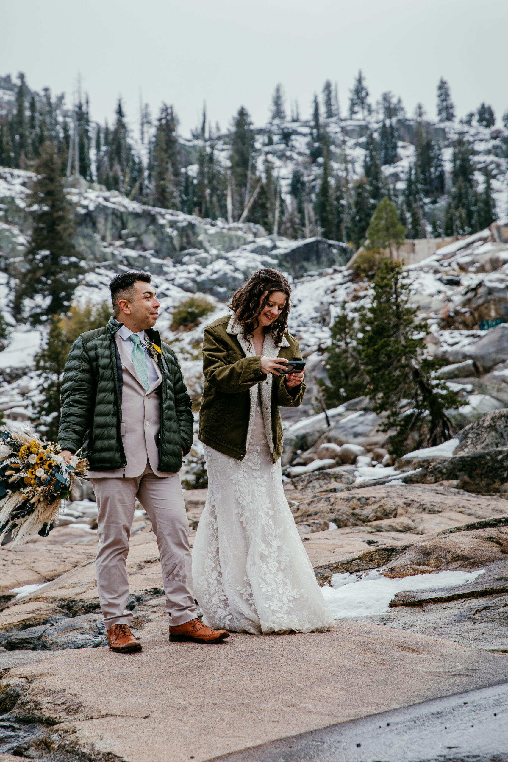 Couple bundled in jackets exploring snowy granite terrain near Donner Summit during their October elopement.