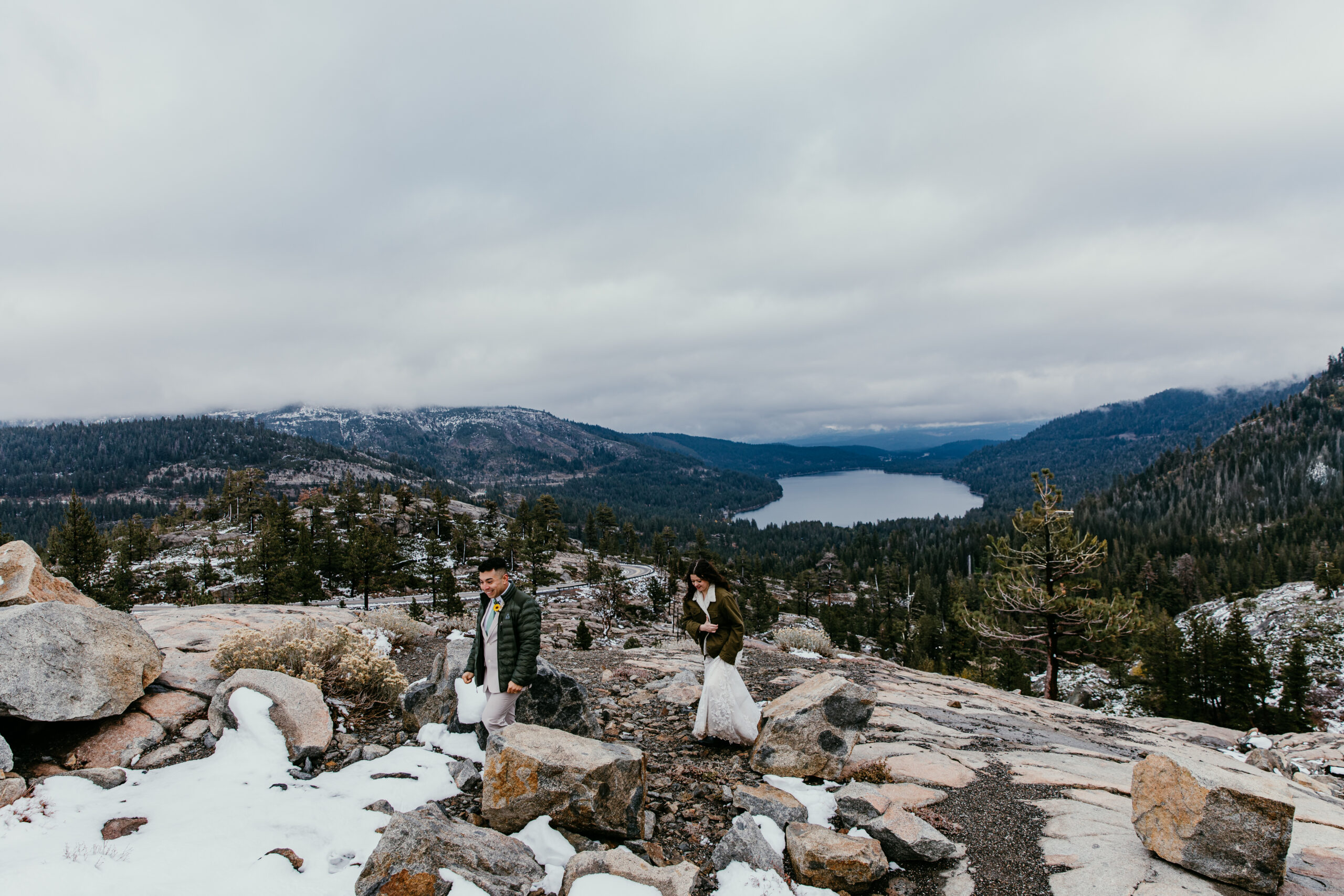Couple hiking across snowy granite with a mountain lake visible below near Donner Summit.