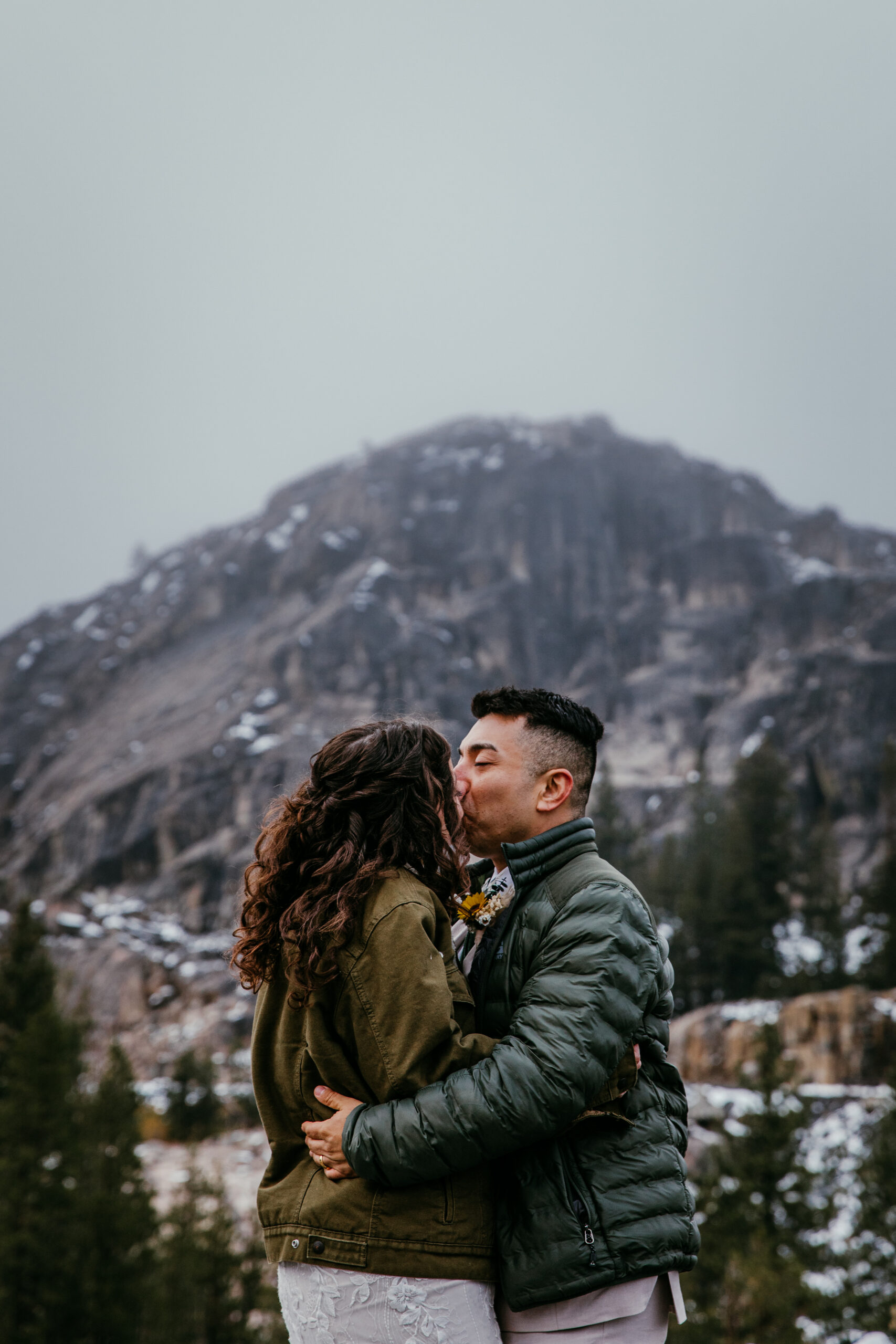 Bride and groom bundled in warm jackets with snow-covered peaks in the background at Donner Summit.
