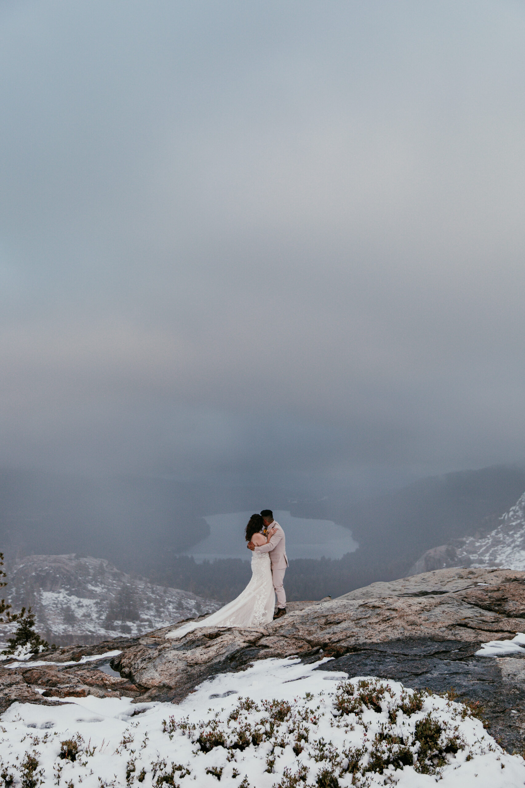 Couple embracing on a foggy mountain overlook with snow-dusted granite and pine trees.