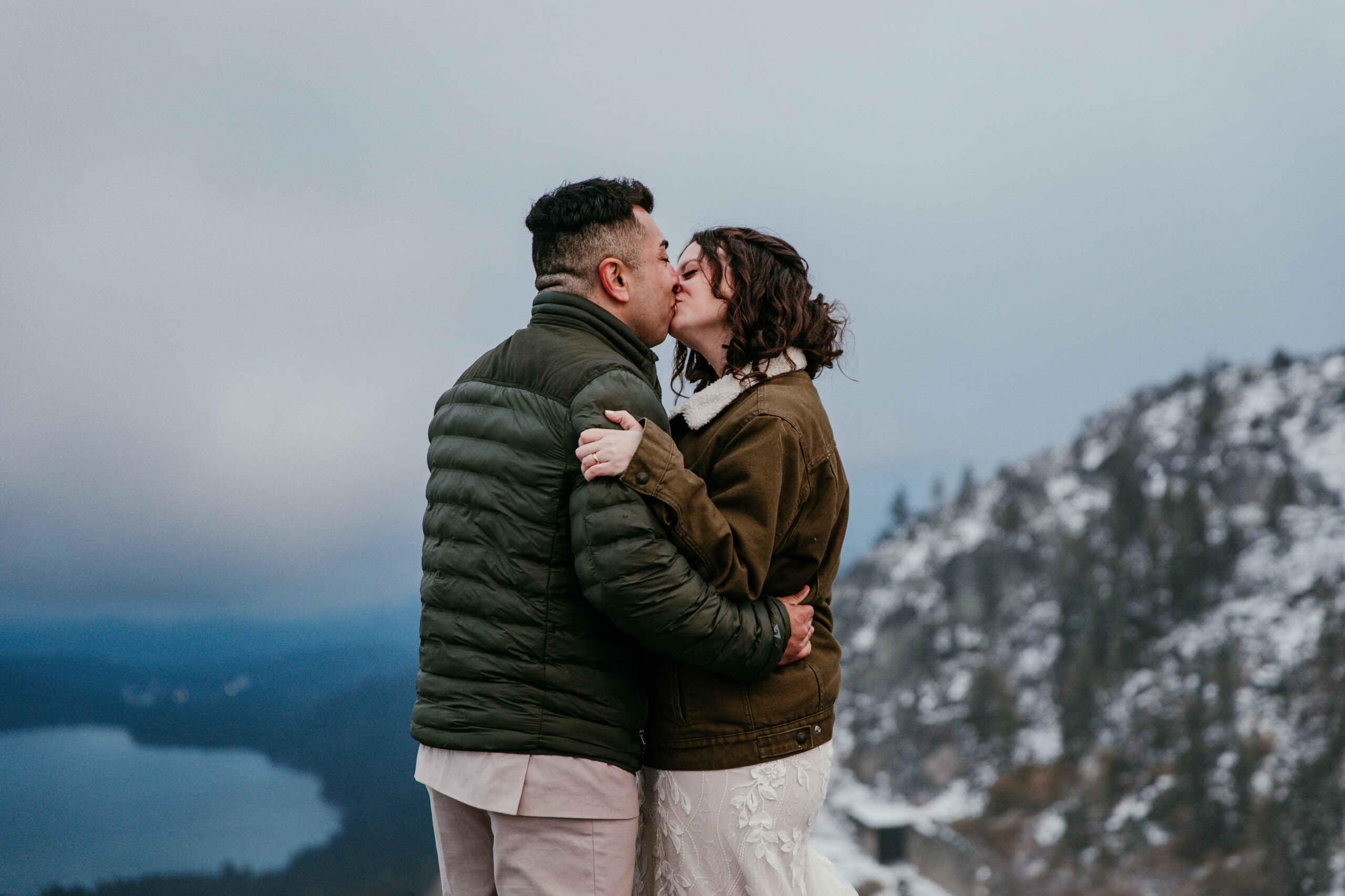 Couple bundled in jackets sharing a kiss on a snowy mountain overlook near Donner Summit.