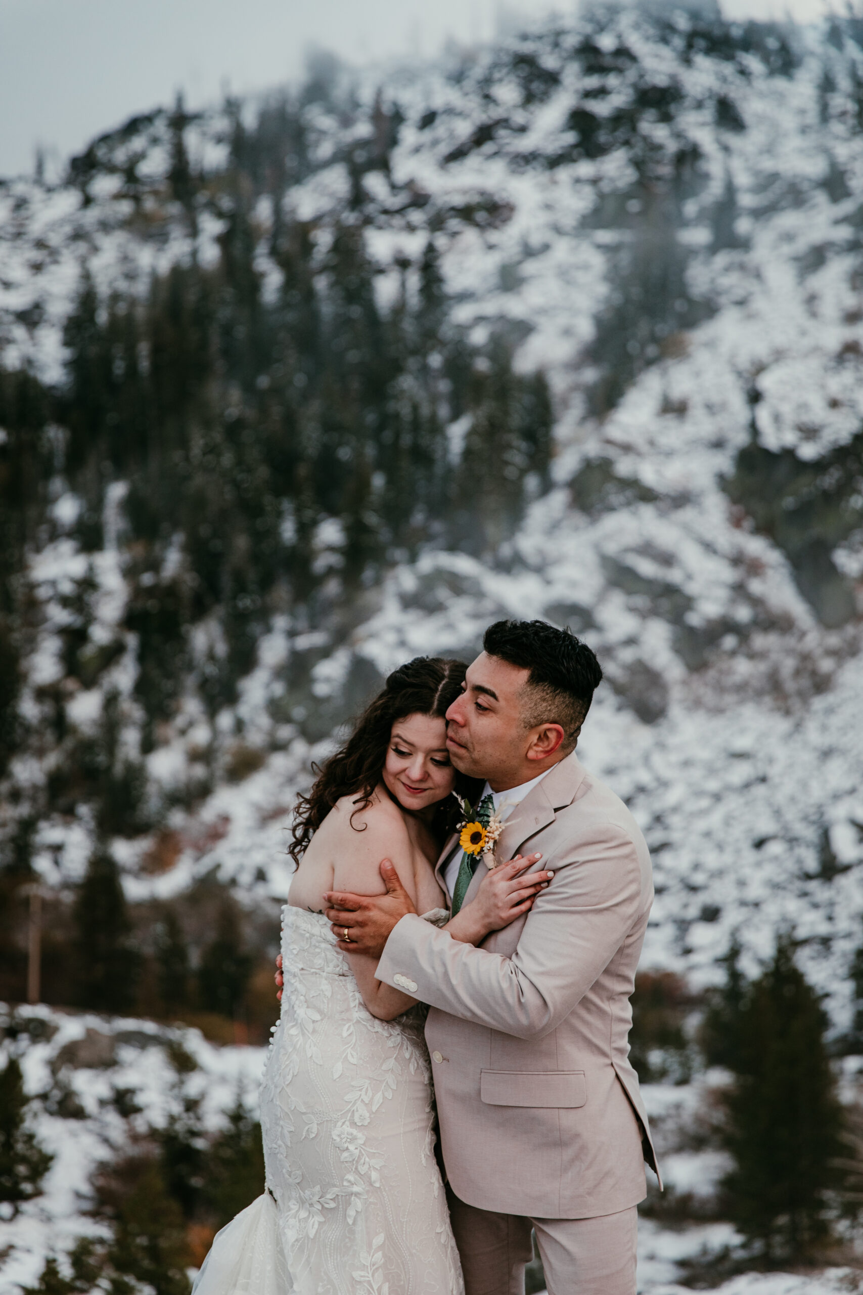 Bride and groom embracing in fresh snowfall on a moody mountain overlook near Donner Summit.