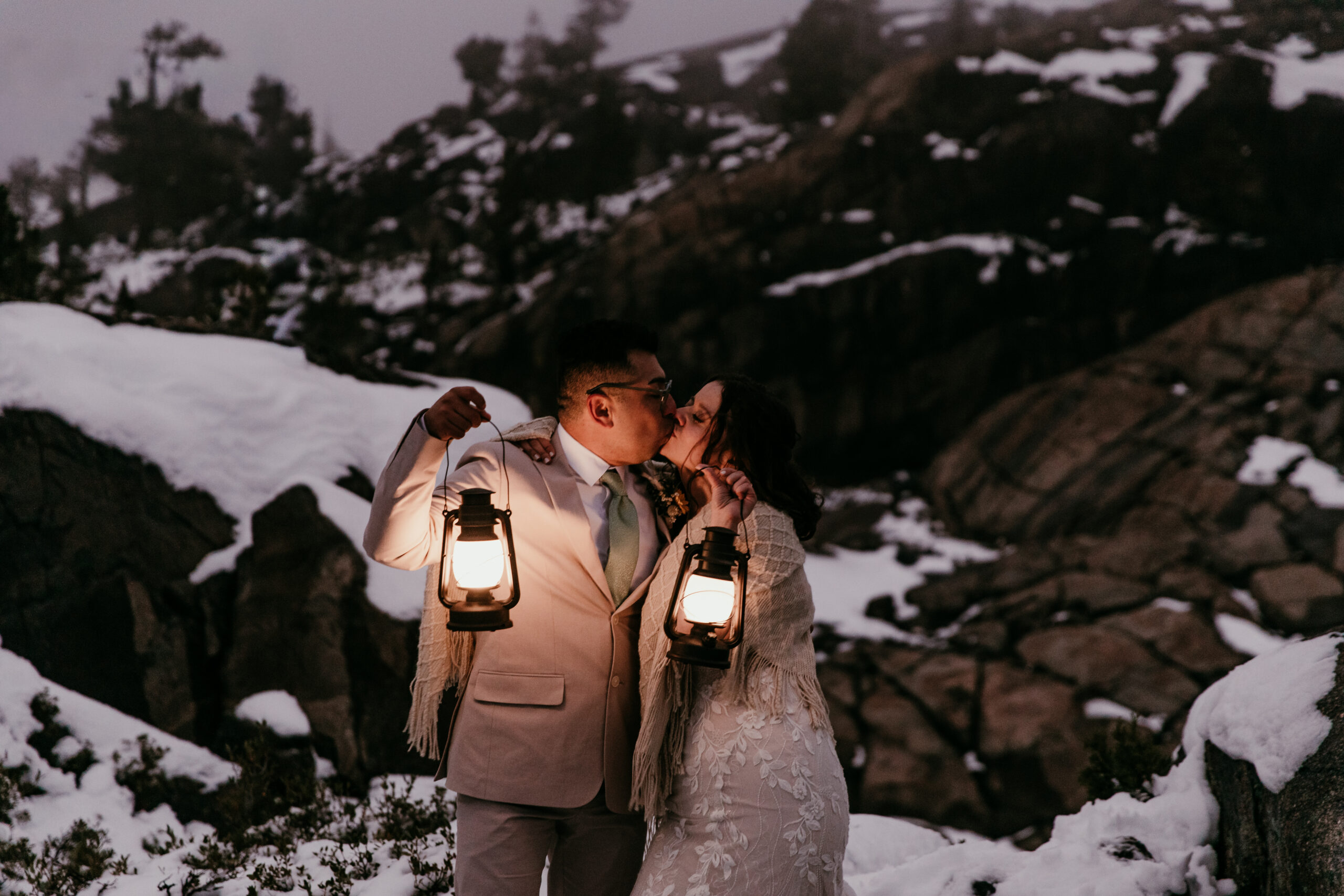 Couple kissing while holding glowing lanterns during a moody blue hour elopement portrait in the mountains.
