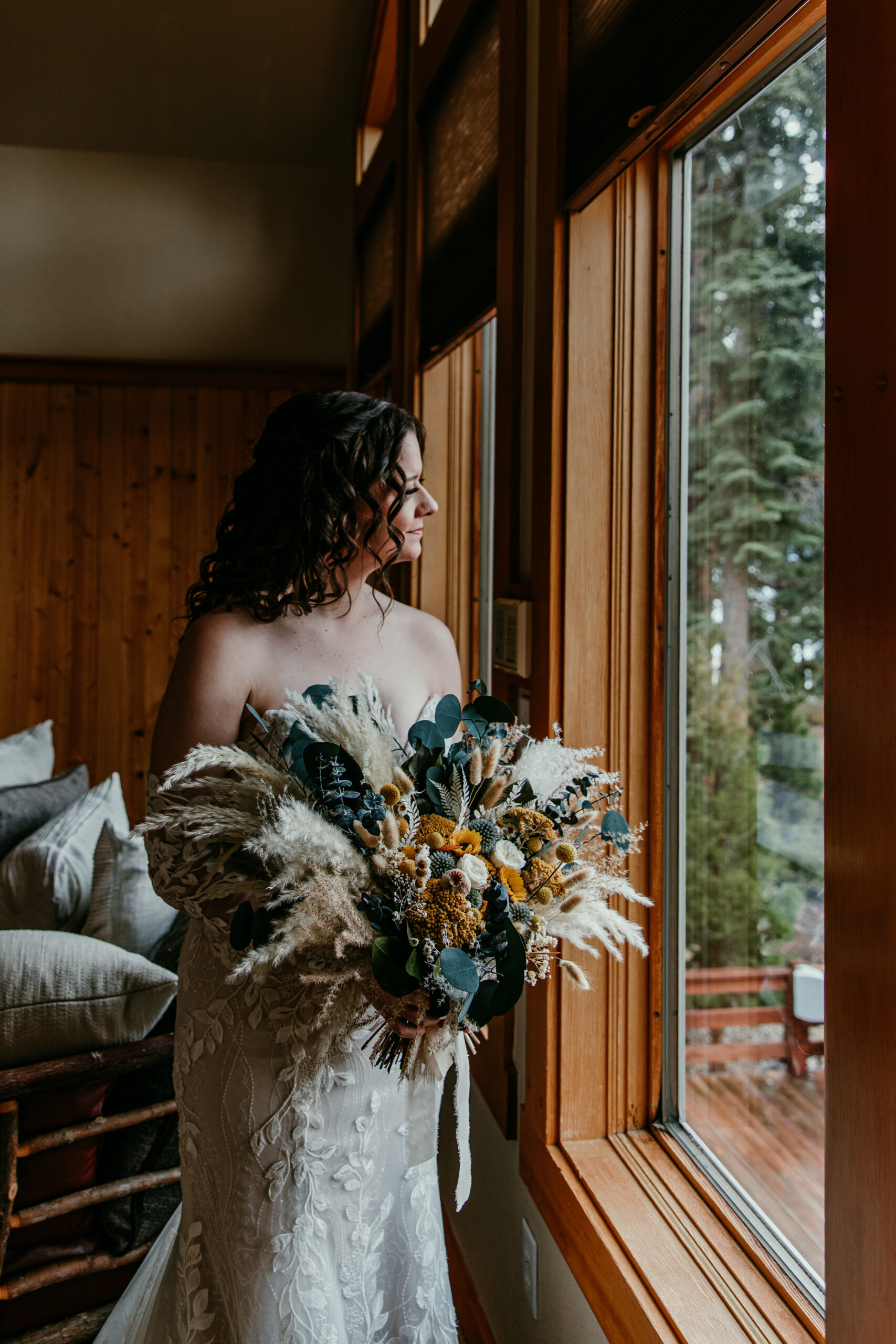 Bride holding her bouquet by the window inside a Lake Tahoe cabin before her intimate elopement ceremony.