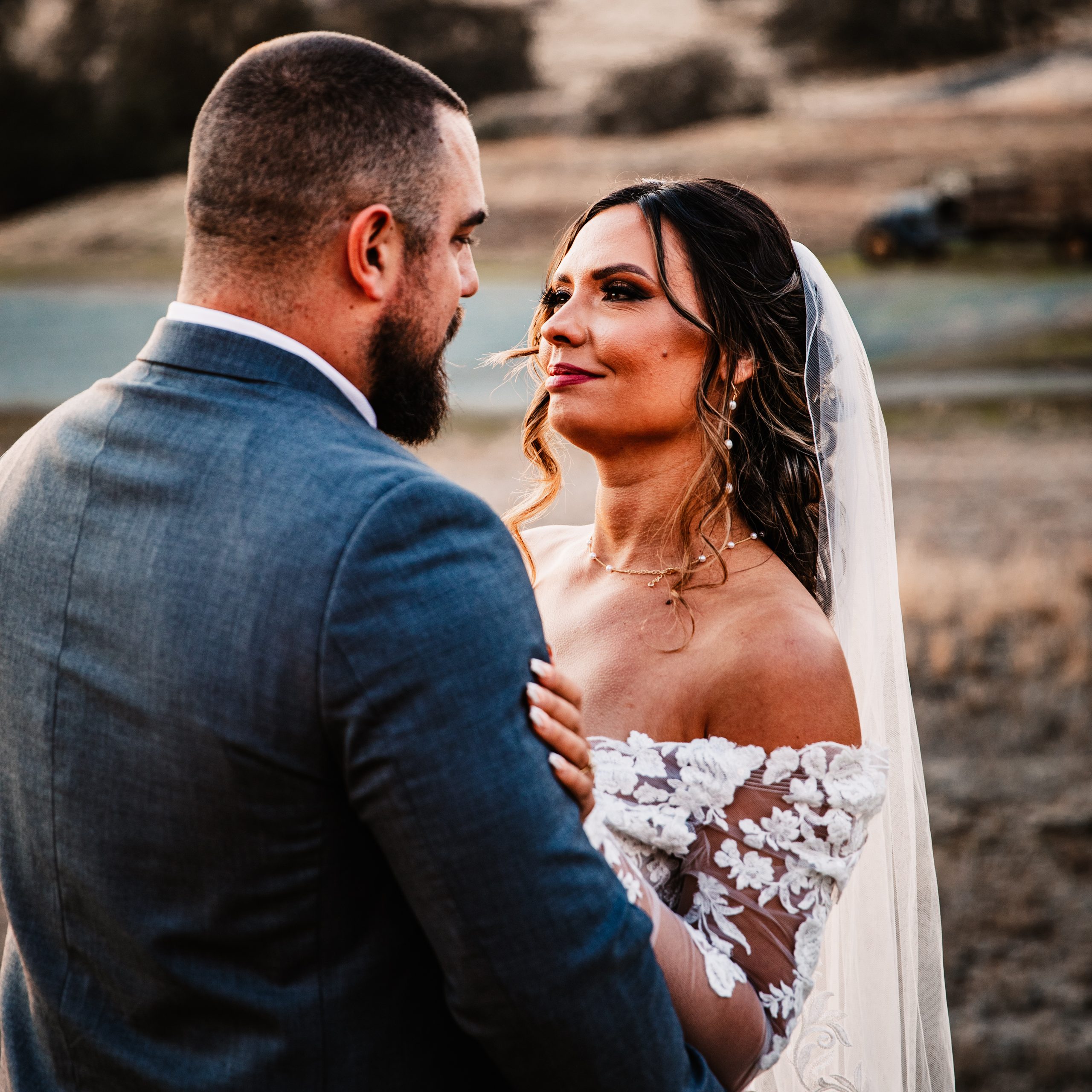 Close-up of a bride in an off-the-shoulder lace dress looking at her groom at Rancho Victoria.