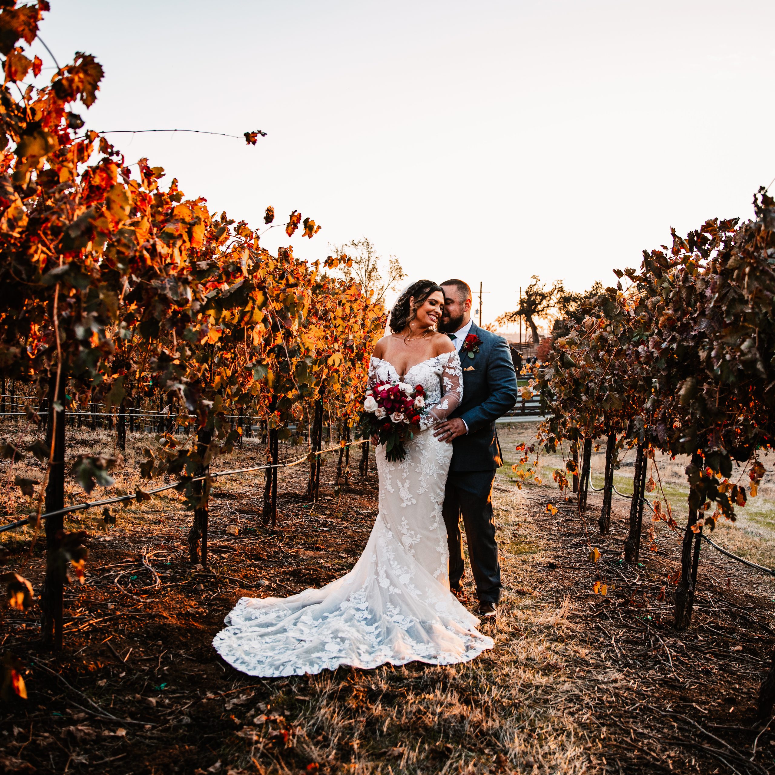 Couple embracing between rows of autumn grapevines at Rancho Victoria in Plymouth.