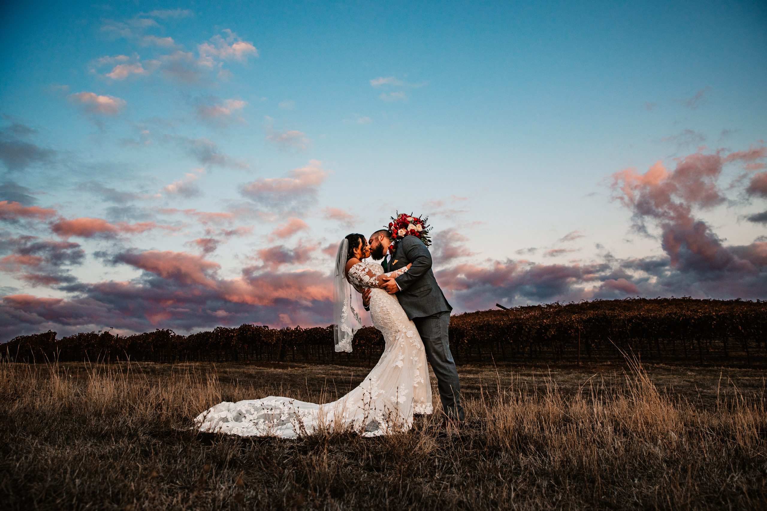 Groom dipping and kissing the bride beneath a colorful evening sky at Rancho Victoria.