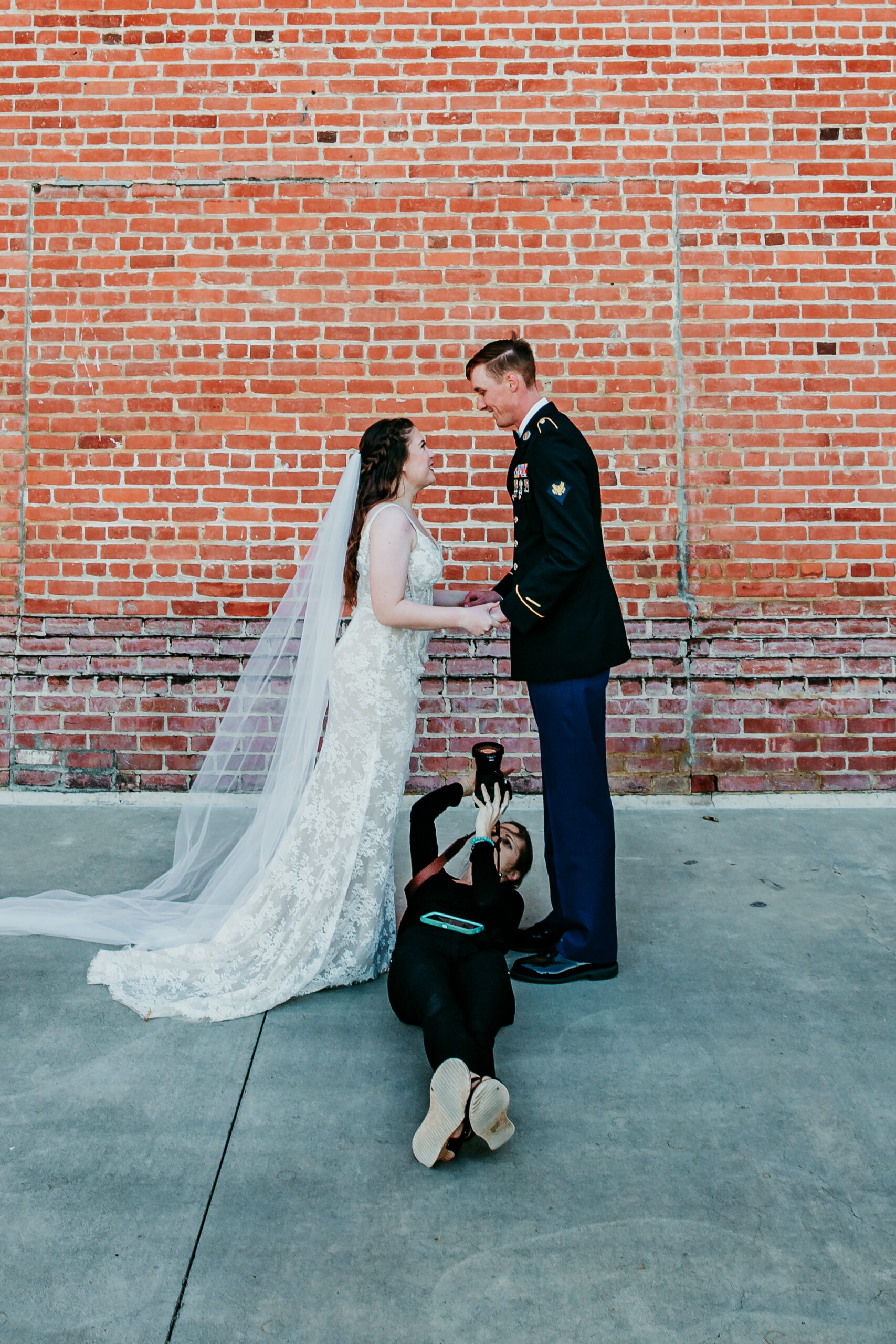 Elopement photographer capturing romantic wedding portraits of a bride and groom against a brick wall.