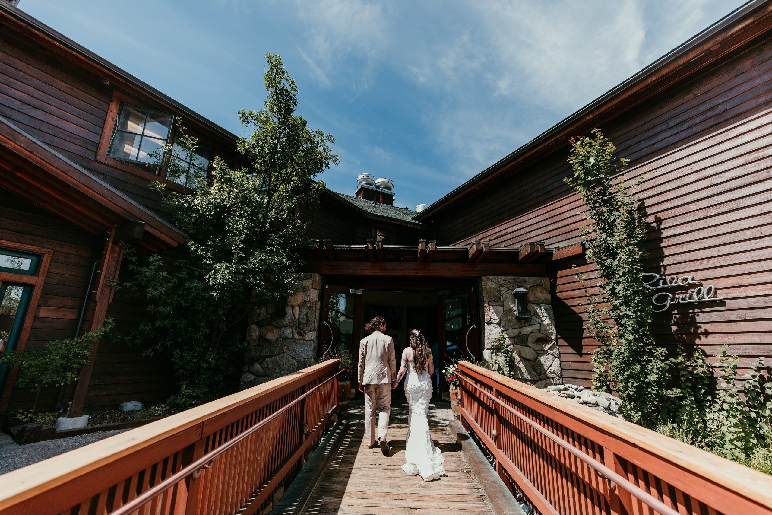 Newlyweds holding hands as they cross a wooden walkway toward Riva Grill in South Lake Tahoe.