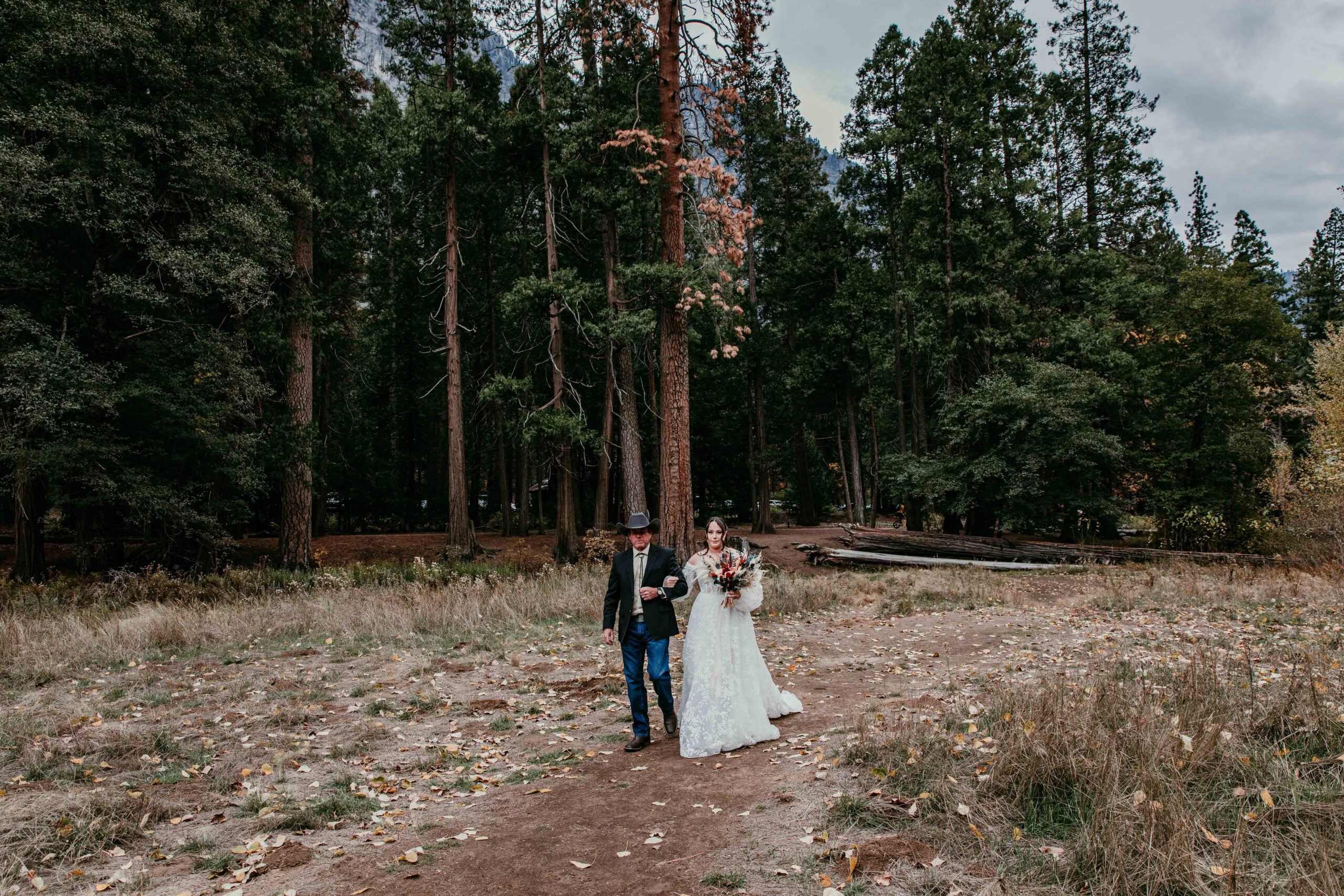 Father of the bride walking the bride through a pine forest surrounded by mountains, one of many peaceful elopement ideas in California