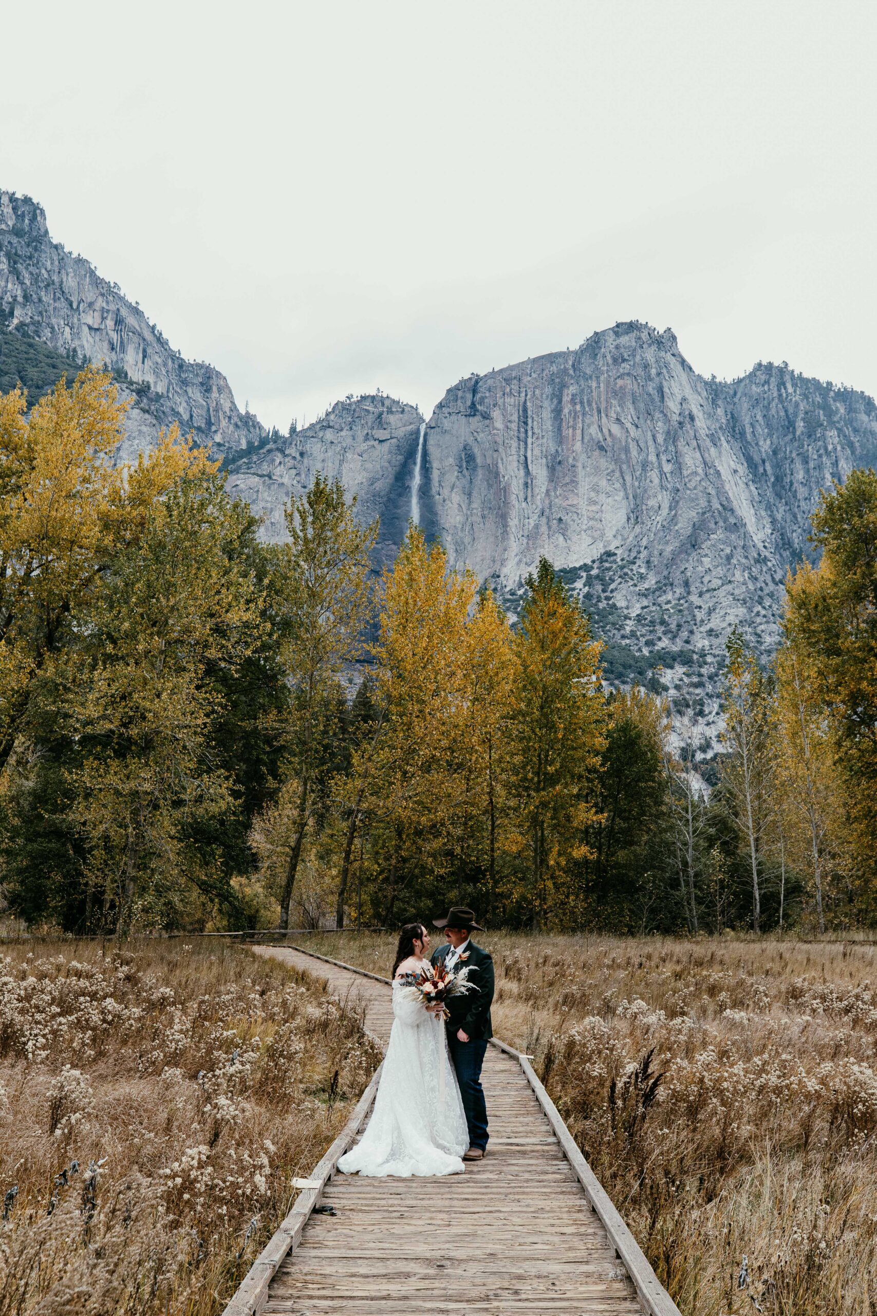 couple standing on boardwalk in Yosemite Valley with Yosemite Falls during a fall elopement in Yosemite