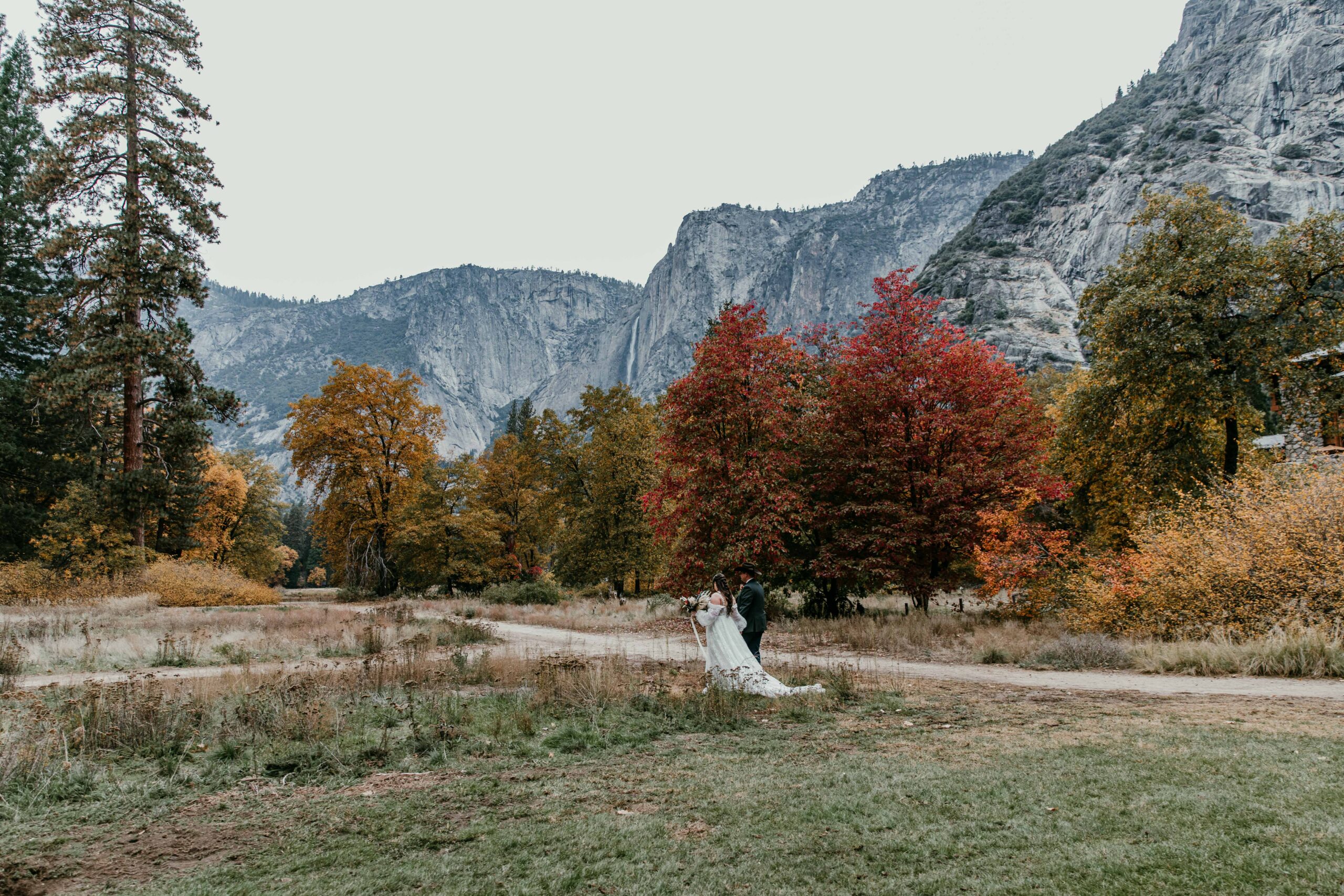 couple surrounded by peak fall colors in Yosemite Valley with Yosemite Falls during a fall elopement in Yosemite