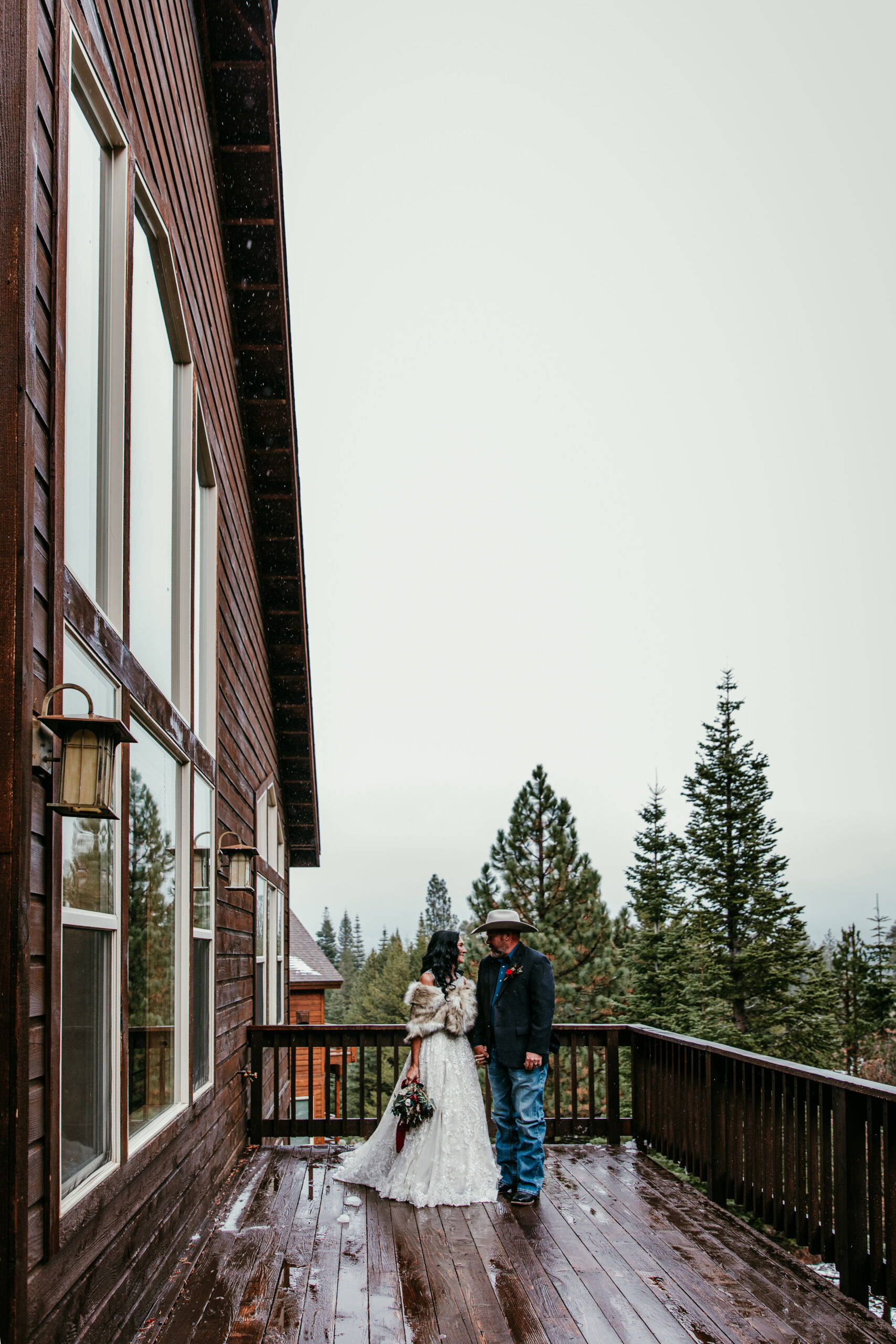 Couple standing on a snowy deck after their small wedding ceremony, cozy mountain cabin setting