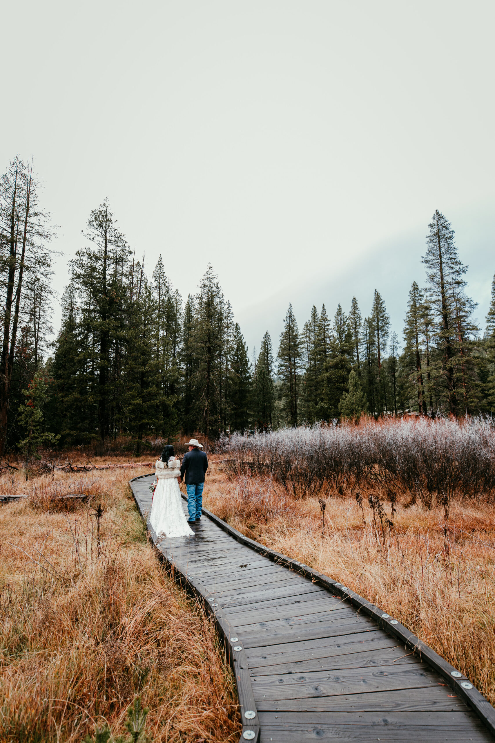 Couple walking along a wooden path after their small wedding in a quiet outdoor setting surrounded by nature