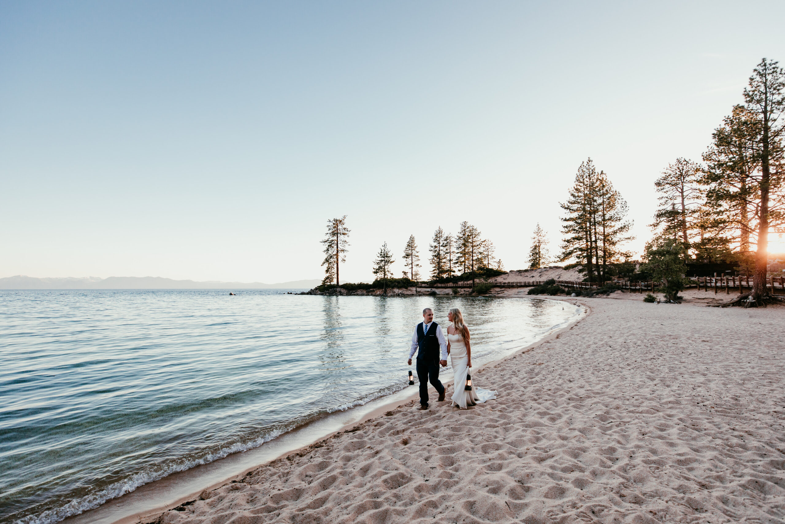 Best Places to Elope in the US featuring a Lake Tahoe elopement with a couple walking along a sandy beach at sunset.
