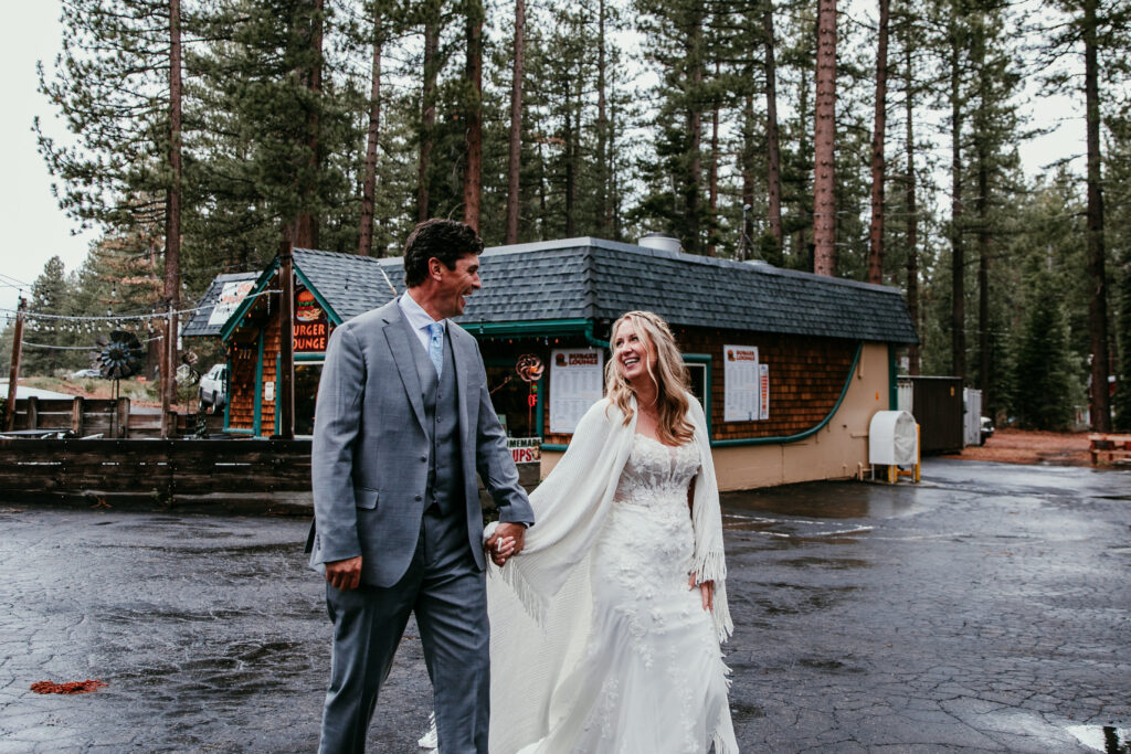 Bride and groom holding hands and laughing outside Burger Lounge during their rainy Lake Tahoe elopement.