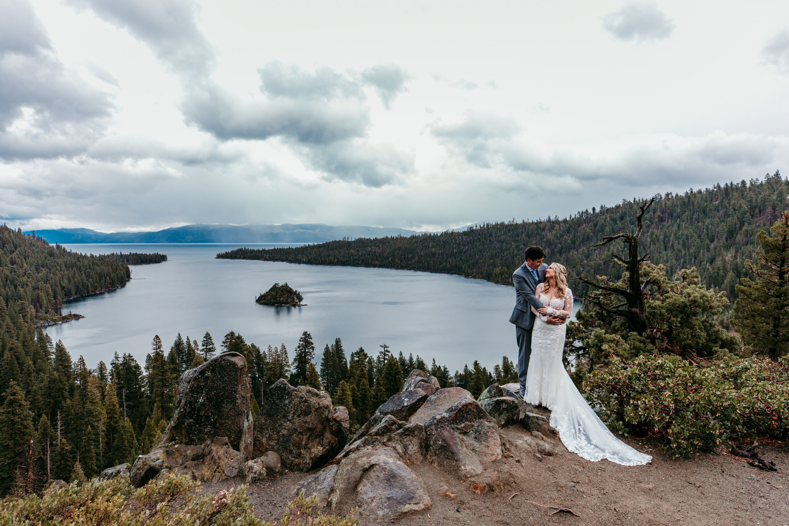 Bride and groom embracing during their rainy Lake Tahoe elopement at Emerald Bay with dramatic storm clouds over Fannette Island.