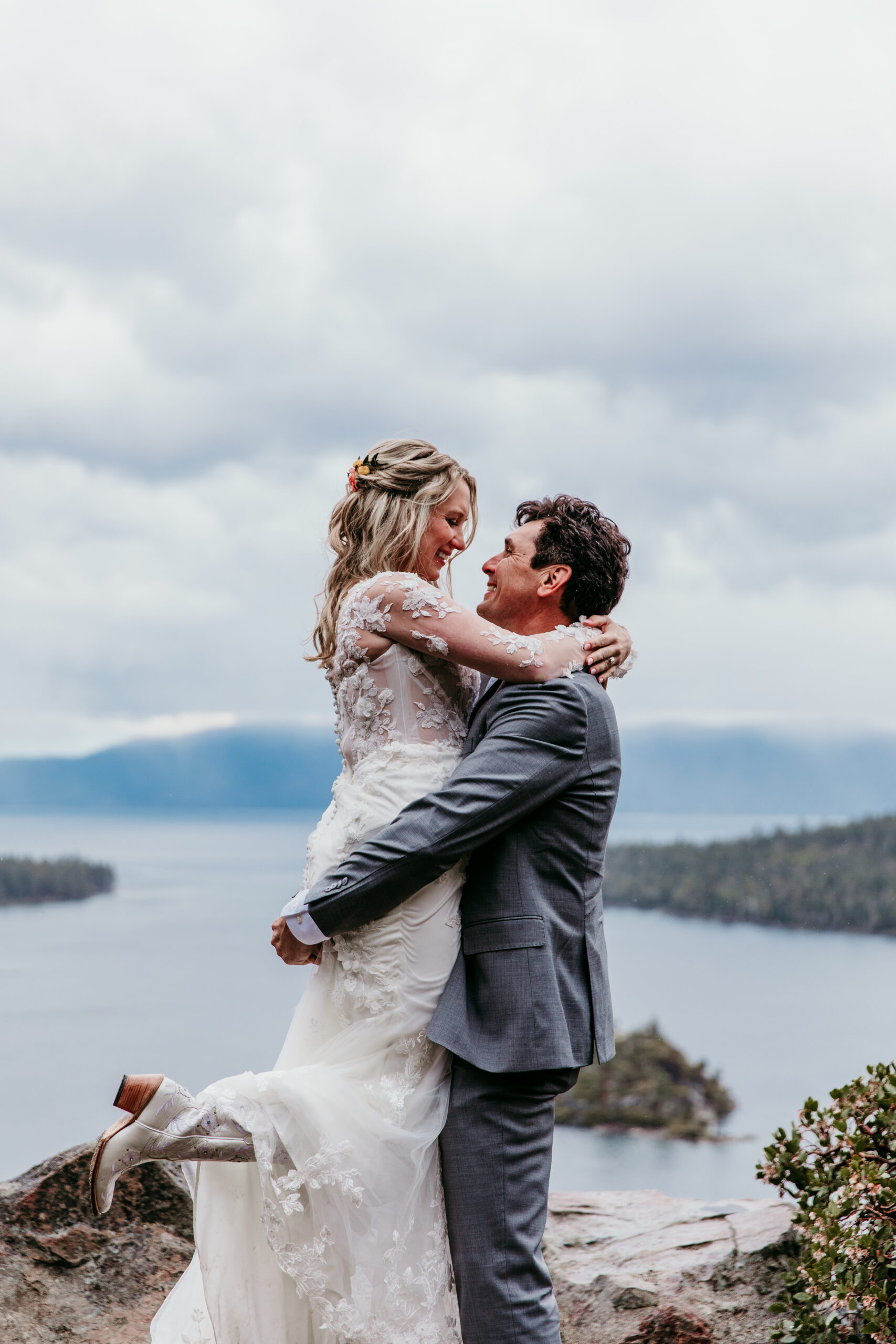 Bride and groom embracing during their rainy Lake Tahoe elopement at Emerald Bay with dramatic storm clouds and Fannette Island in the background.
