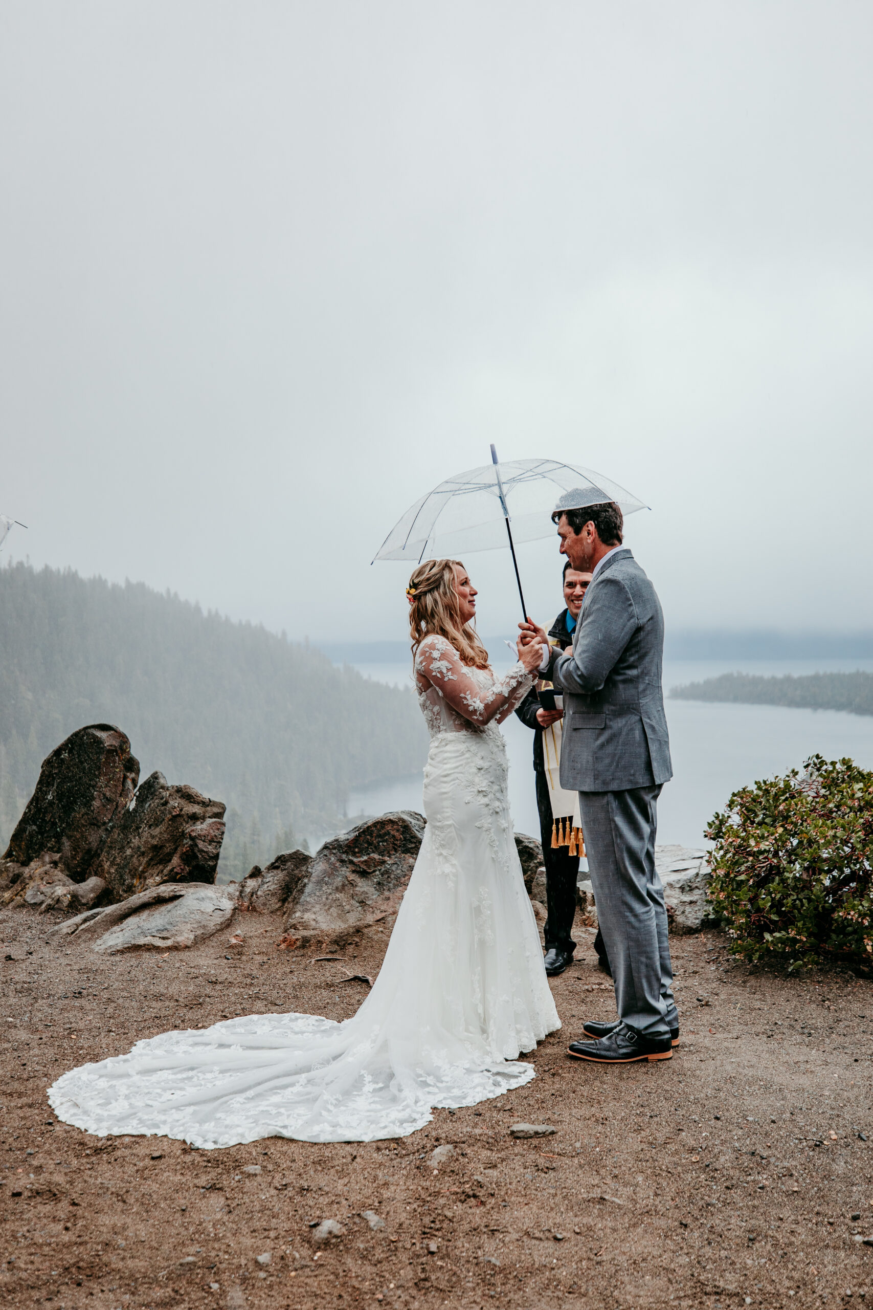 Bride and groom exchanging heartfelt vows beneath a clear umbrella during their rainy Lake Tahoe elopement ceremony at Emerald Bay.