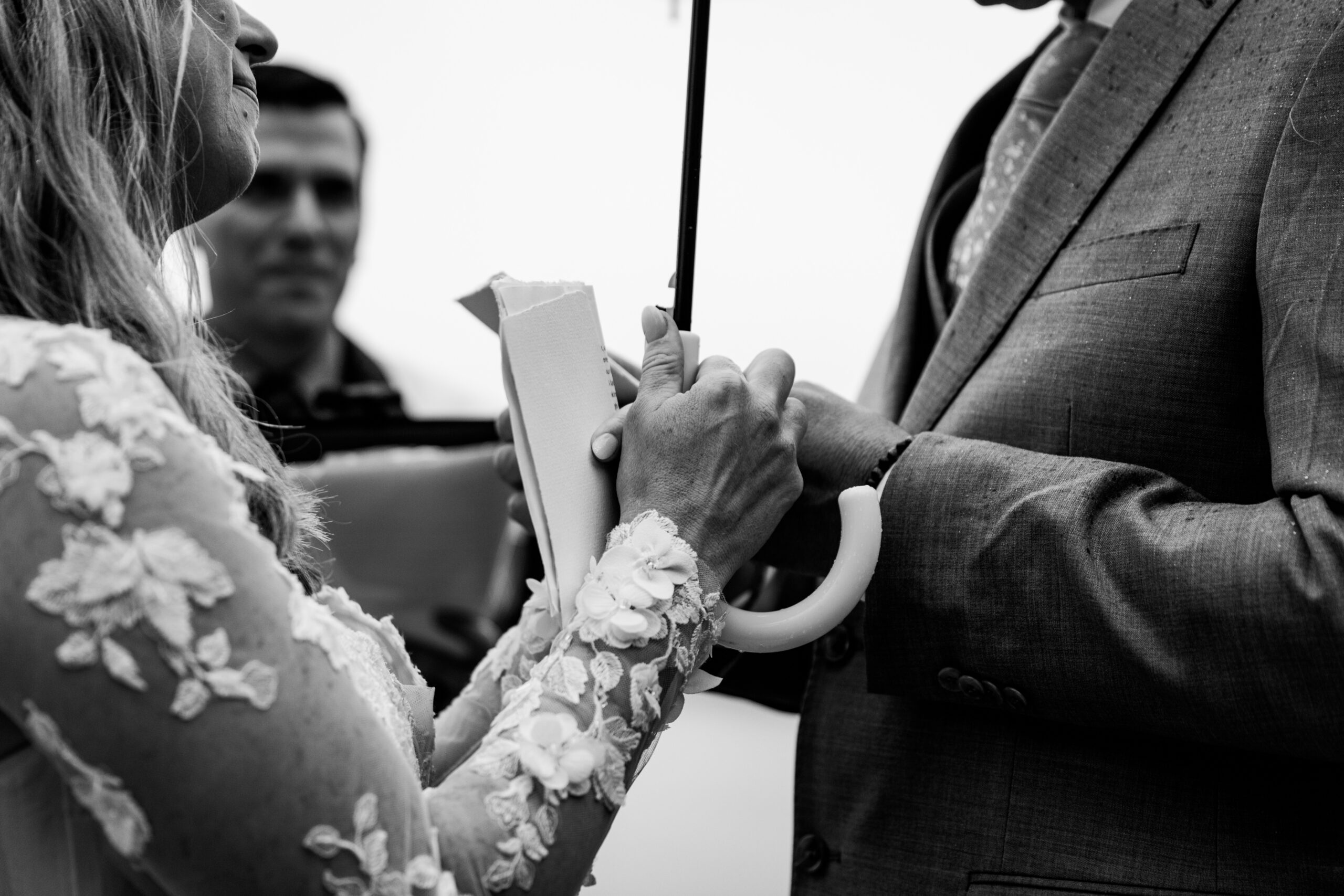 Black and white close-up of the bride and groom holding hands during their rainy Lake Tahoe elopement ceremony at Emerald Bay.