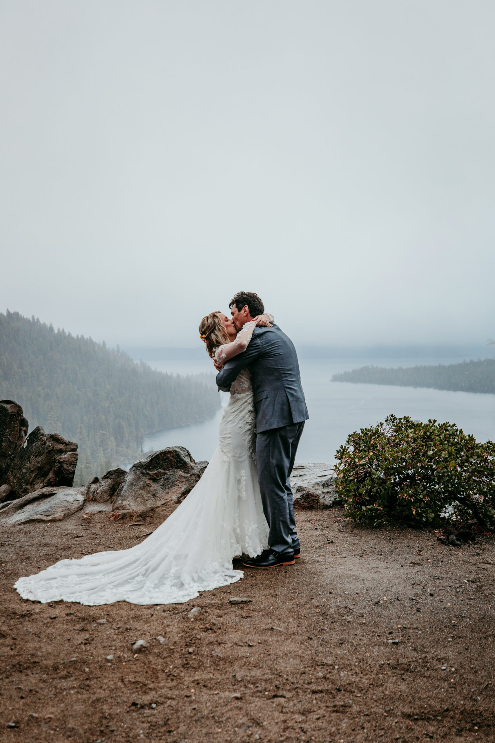 Bride and groom sharing their first kiss after their rainy Lake Tahoe elopement ceremony at Emerald Bay with fog covering the lake.