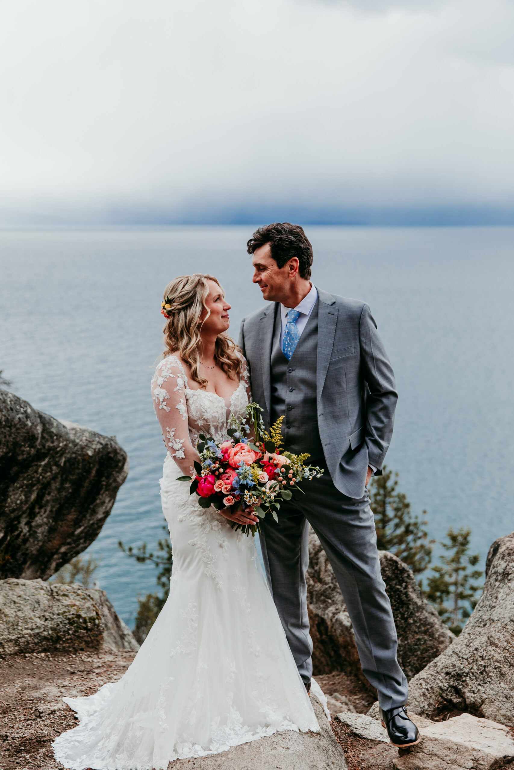 Bride and groom with colorful wedding bouquet overlooking Emerald Bay during their rainy Lake Tahoe elopement.