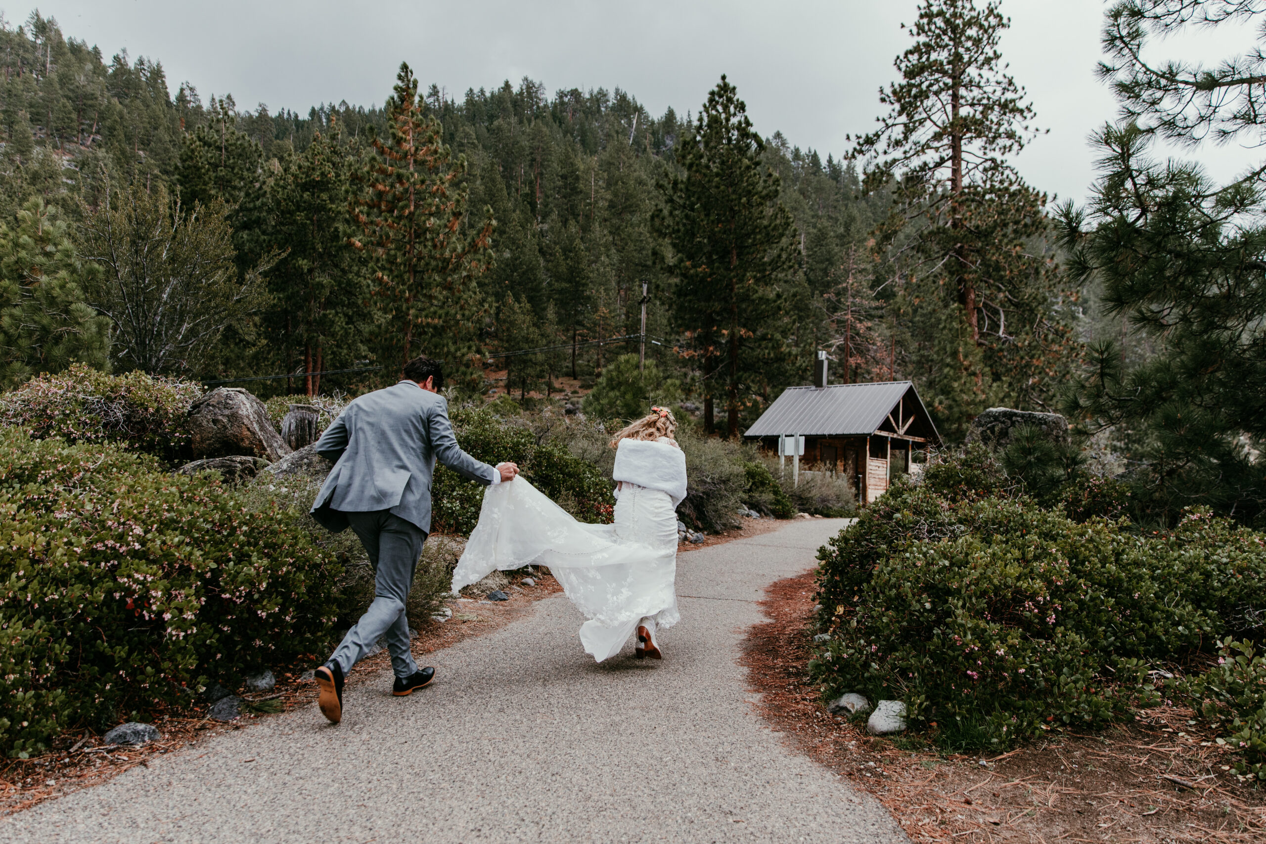 Bride and groom running hand in hand after their rainy Lake Tahoe elopement ceremony at Emerald Bay, wrapped in a blanket to stay warm.