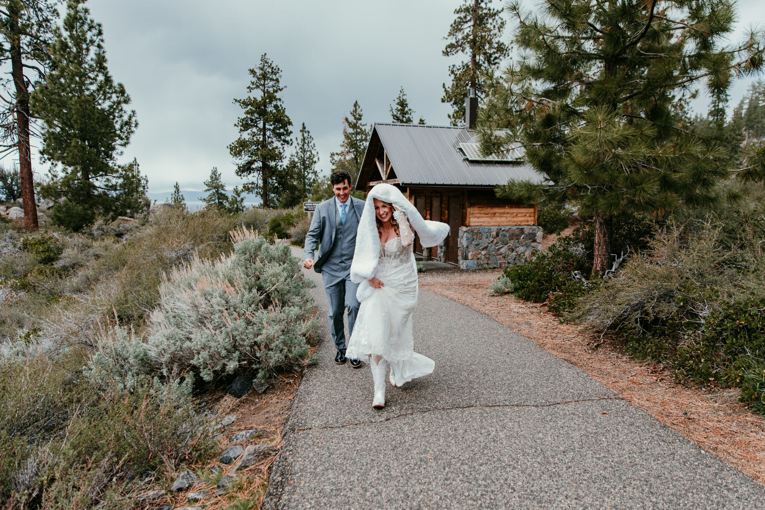 Bride and groom running along the path after their rainy Lake Tahoe elopement ceremony at Emerald Bay, wrapped in a blanket to stay warm.