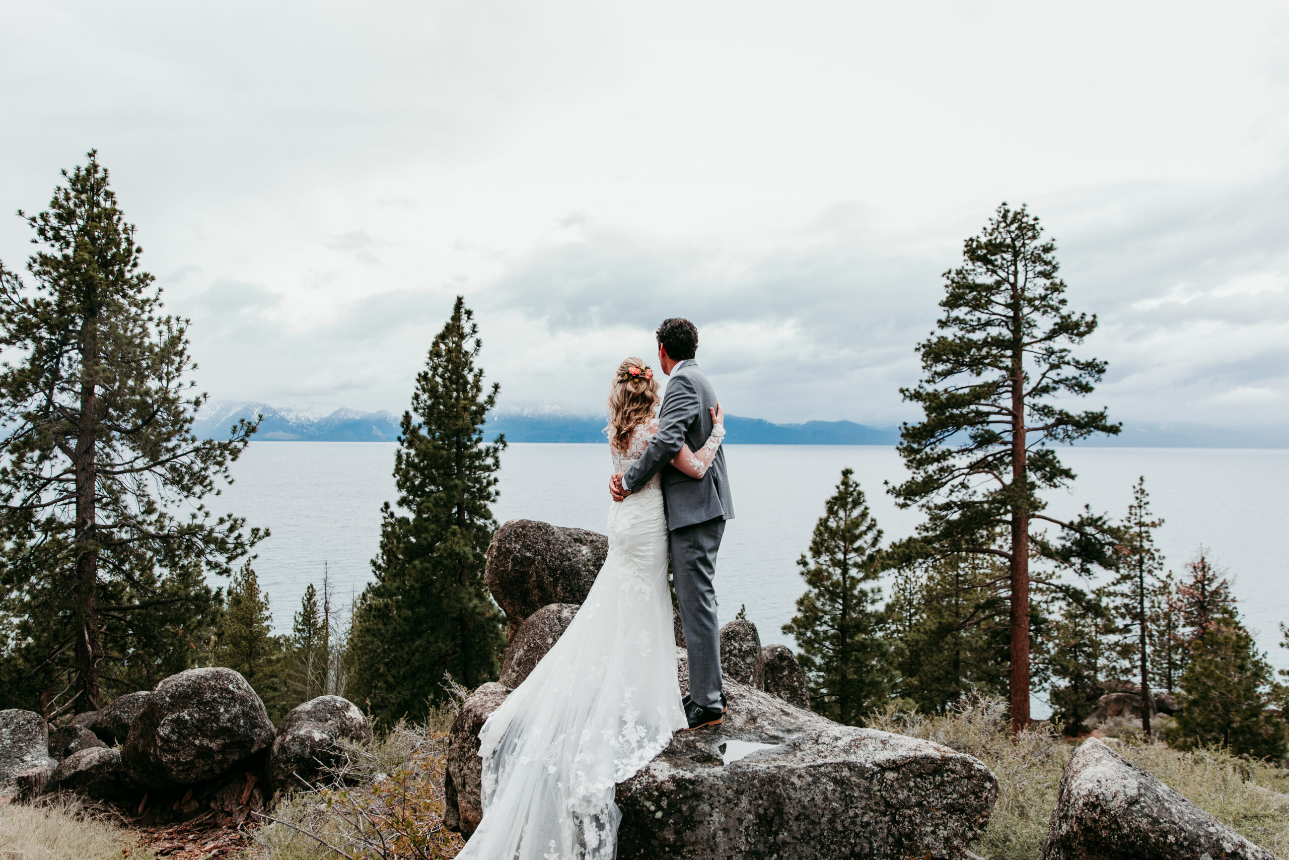 Bride and groom overlooking Lake Tahoe after their rainy Lake Tahoe elopement at Emerald Bay beneath dramatic storm clouds.