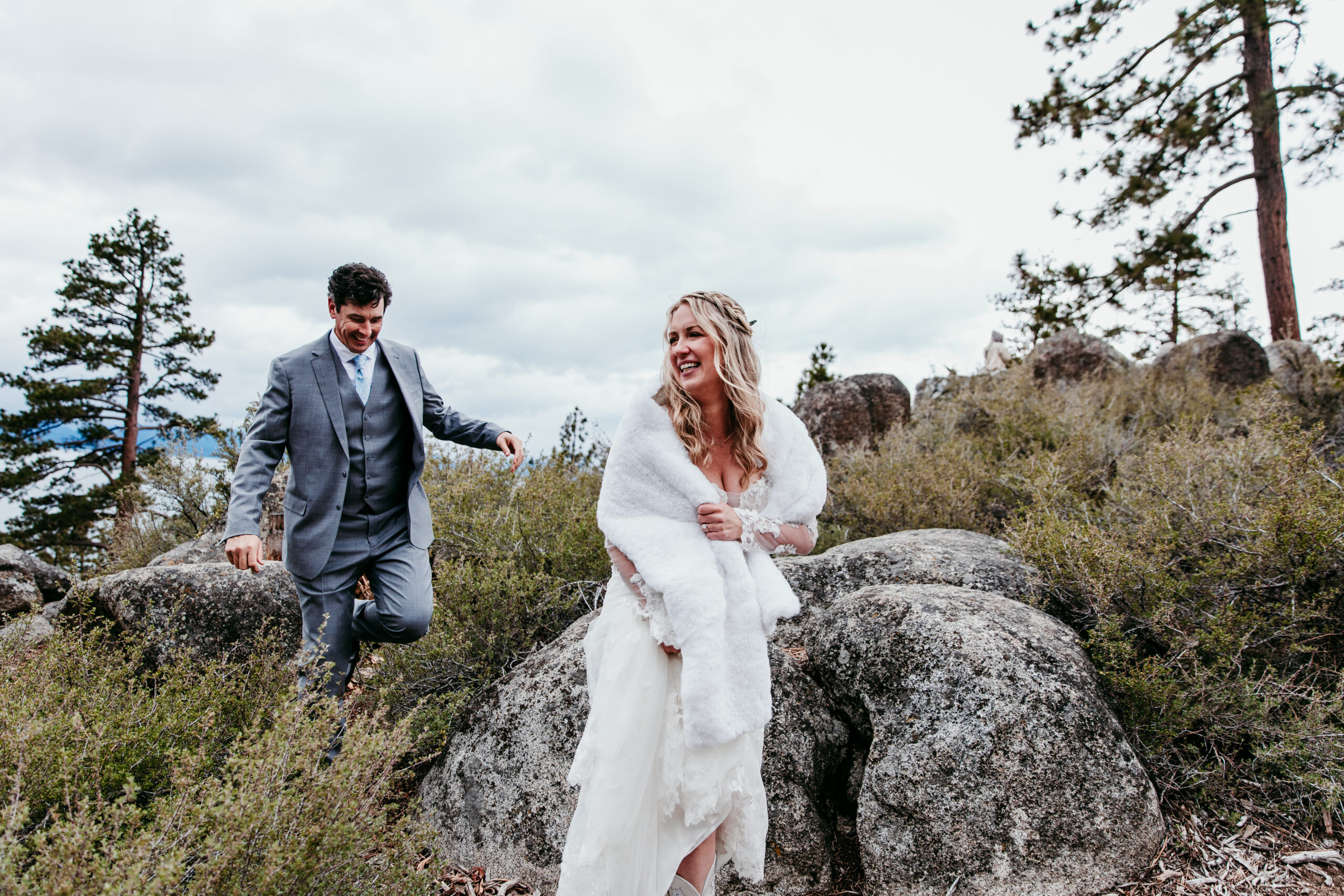 Bride and groom carefully climbing over granite boulders during their rainy Lake Tahoe elopement at Emerald Bay.
