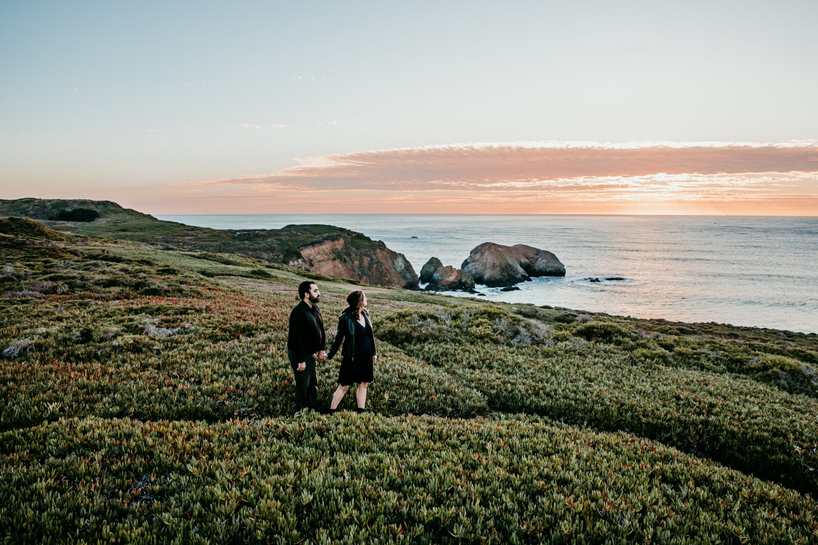 Elopement couple holding hands on a coastal hillside overlooking the ocean at Marin Headlands during sunset.