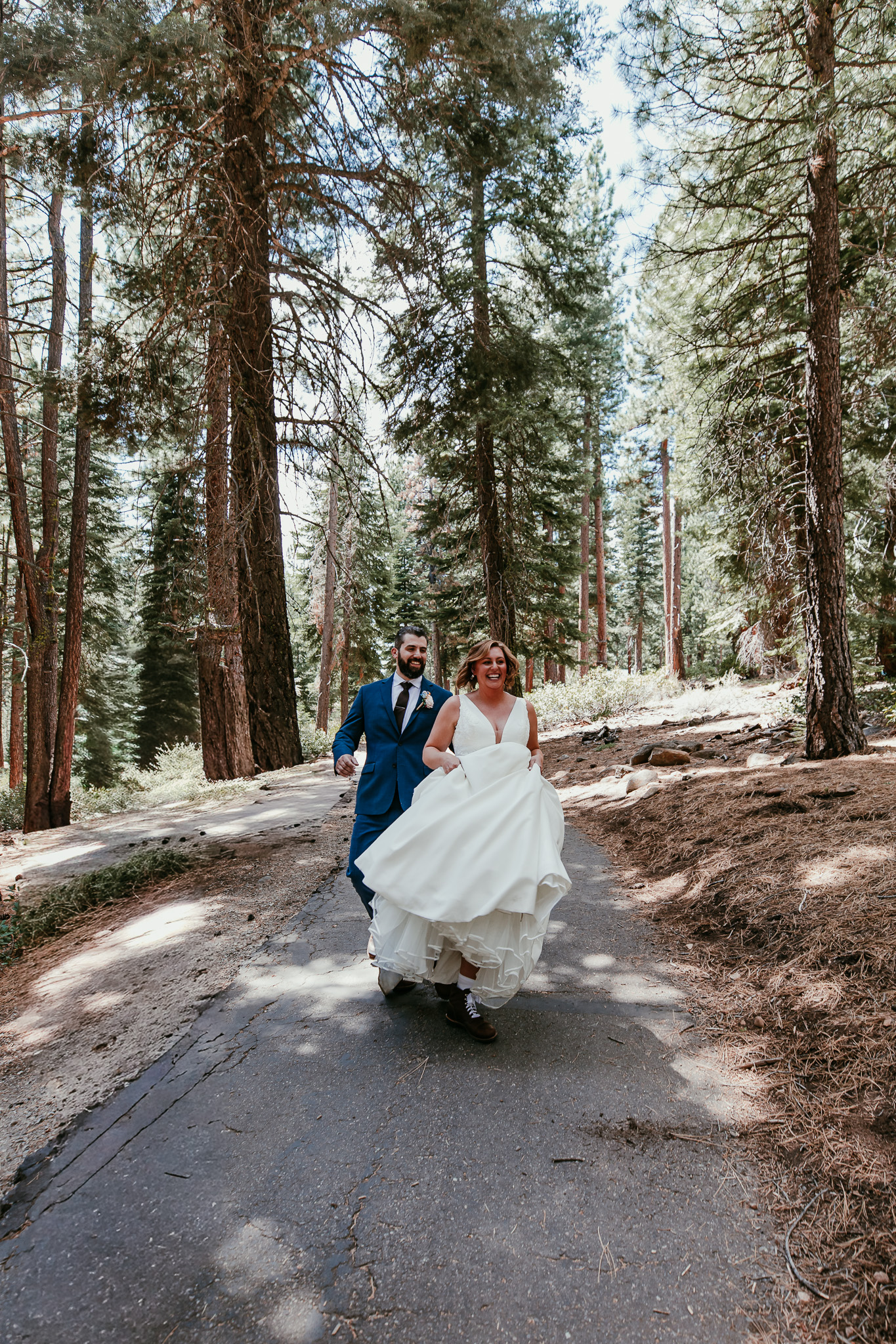 Newlyweds holding hands and walking toward the camera along a forest path in Lake Tahoe.