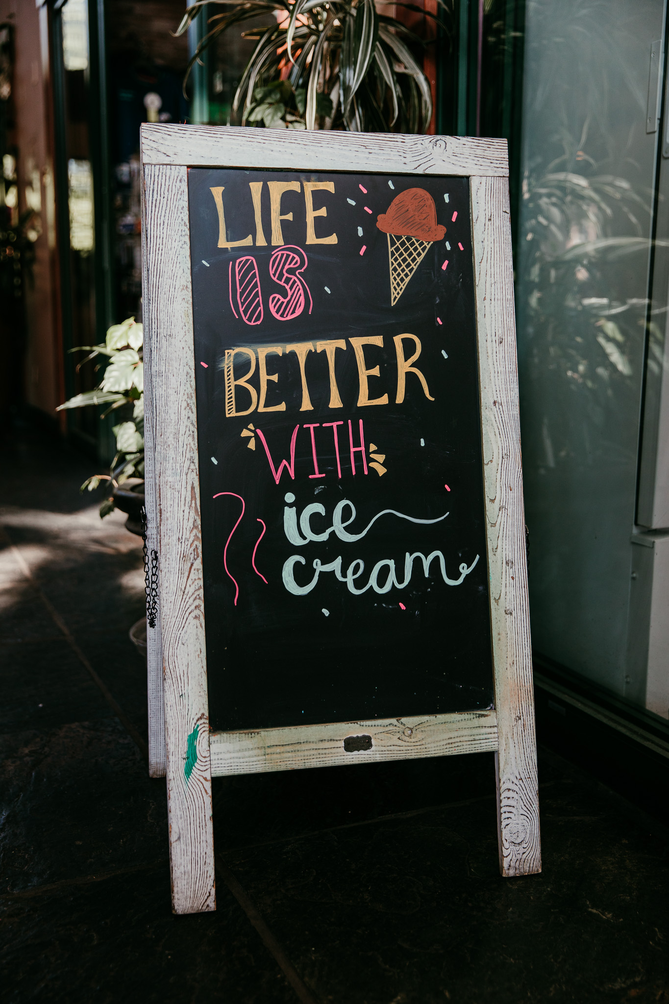 Sidewalk sign reading “Life is better with ice cream” outside an ice cream shop.